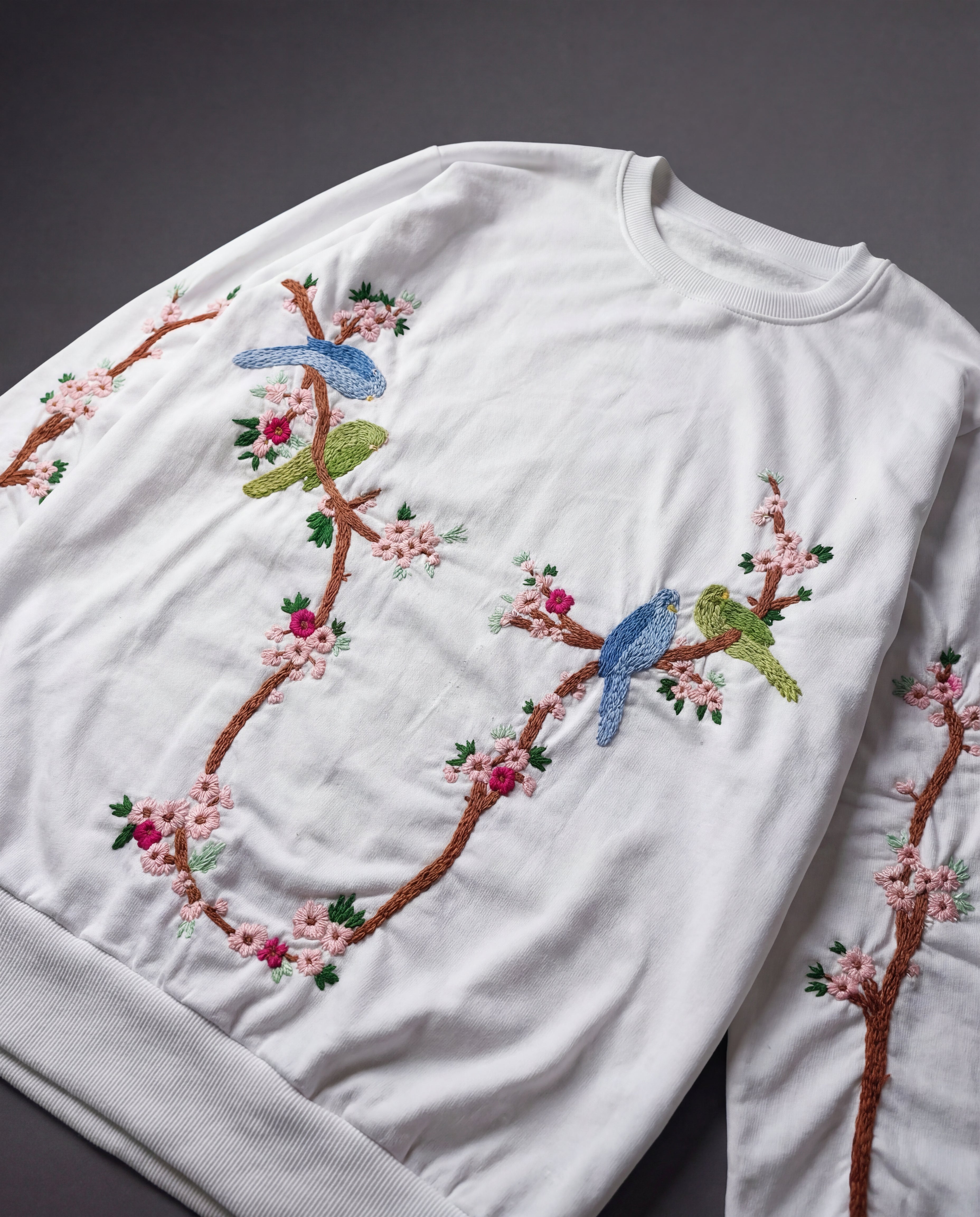 White sweatshirt with embroidered birds and floral branches on a dark background