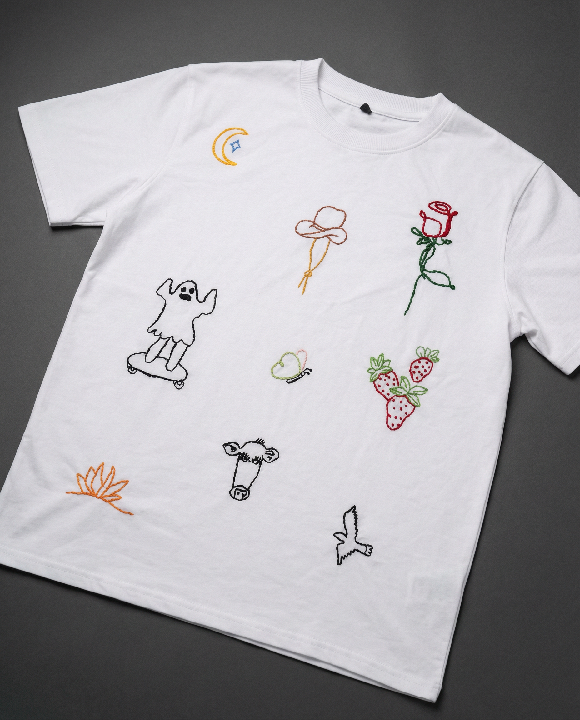 White t-shirt with colorful embroidered designs on a dark background