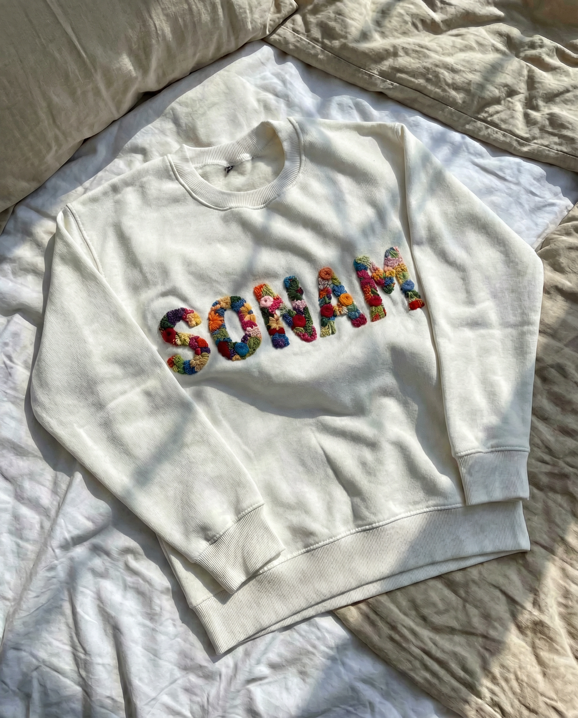 White sweatshirt with custom name hand embroidered  'Soulam' text on a bed