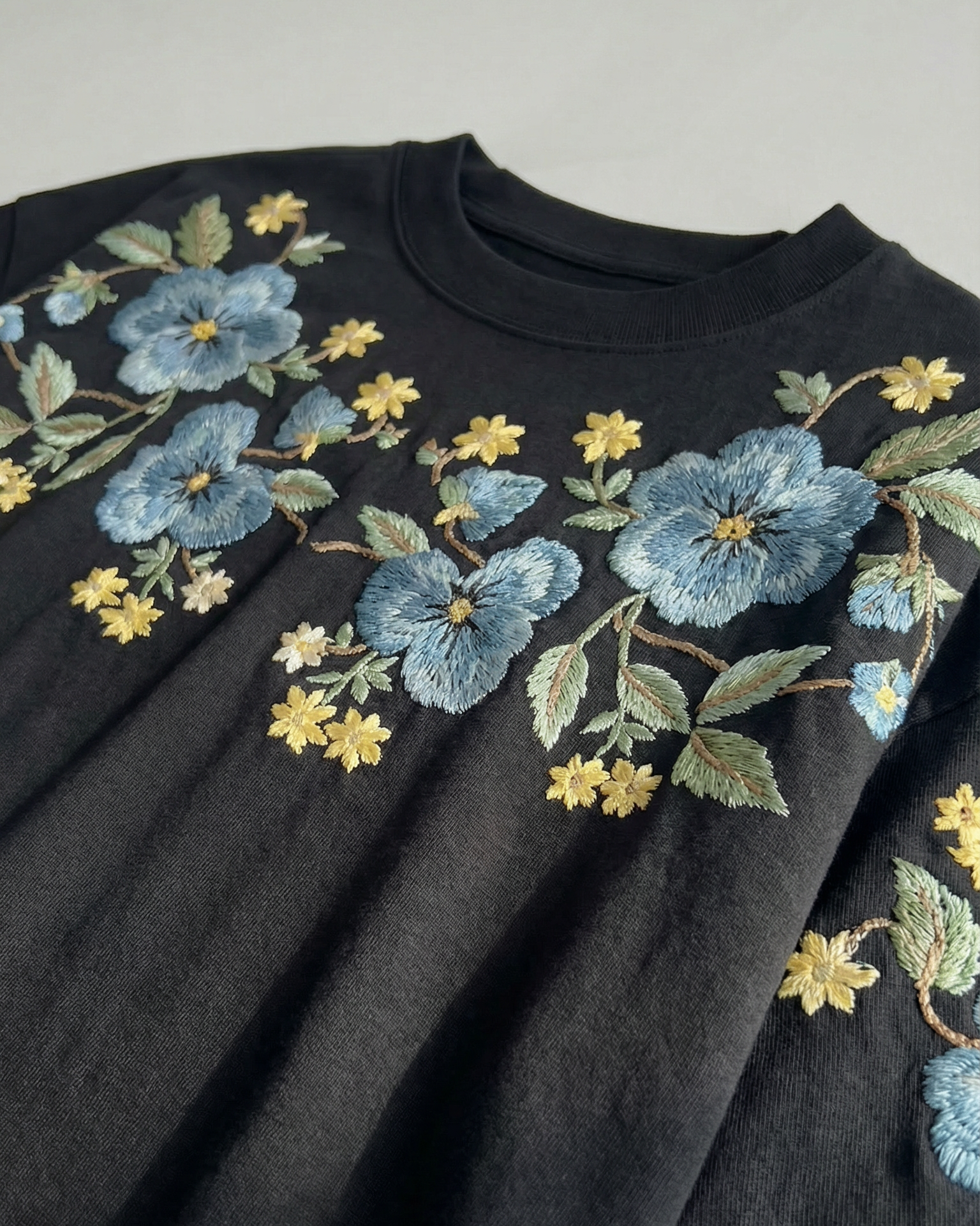 Black sweater with blue floral embroidery on a gray background