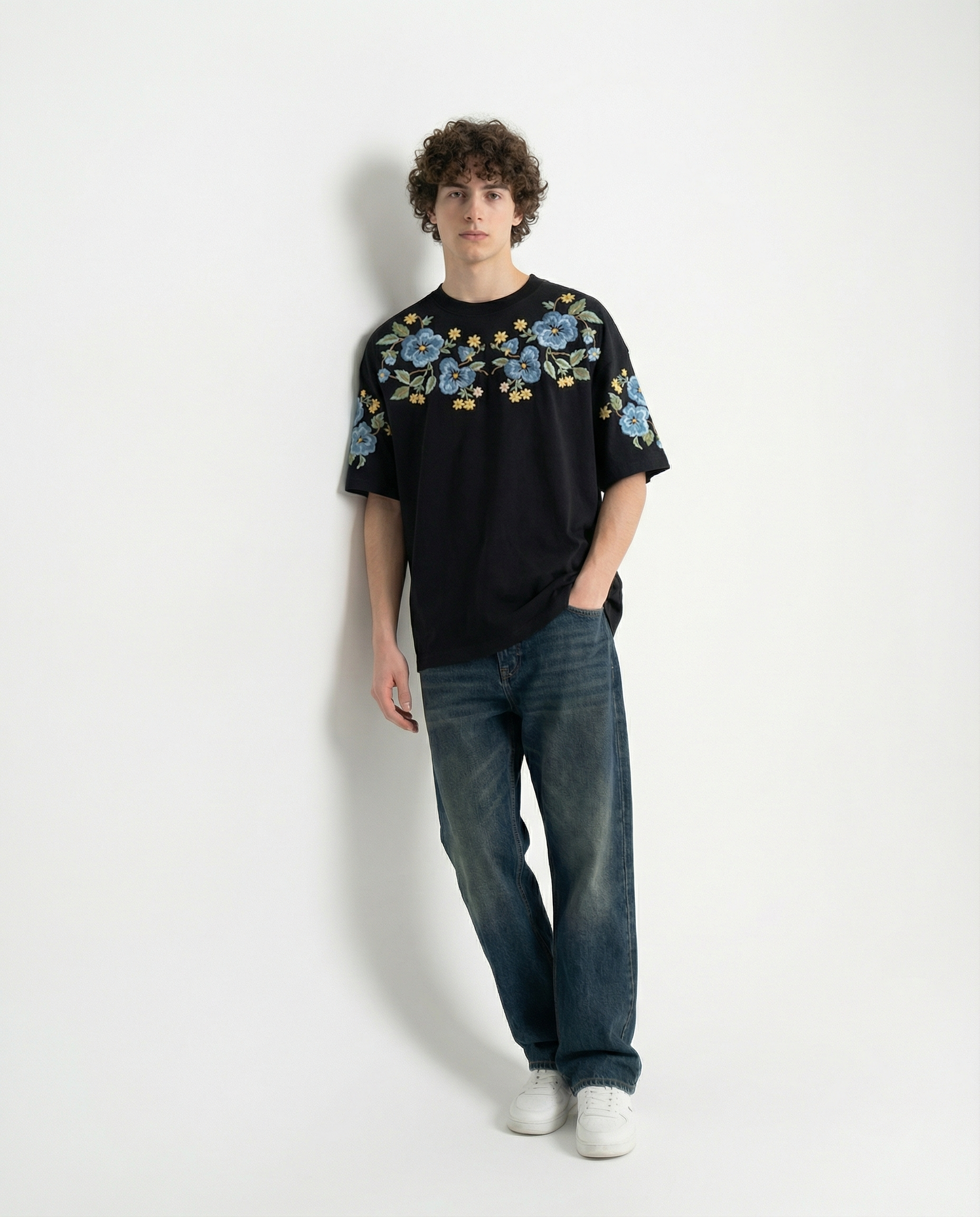 Person wearing a black t-shirt with floral designs and blue jeans on a white background
