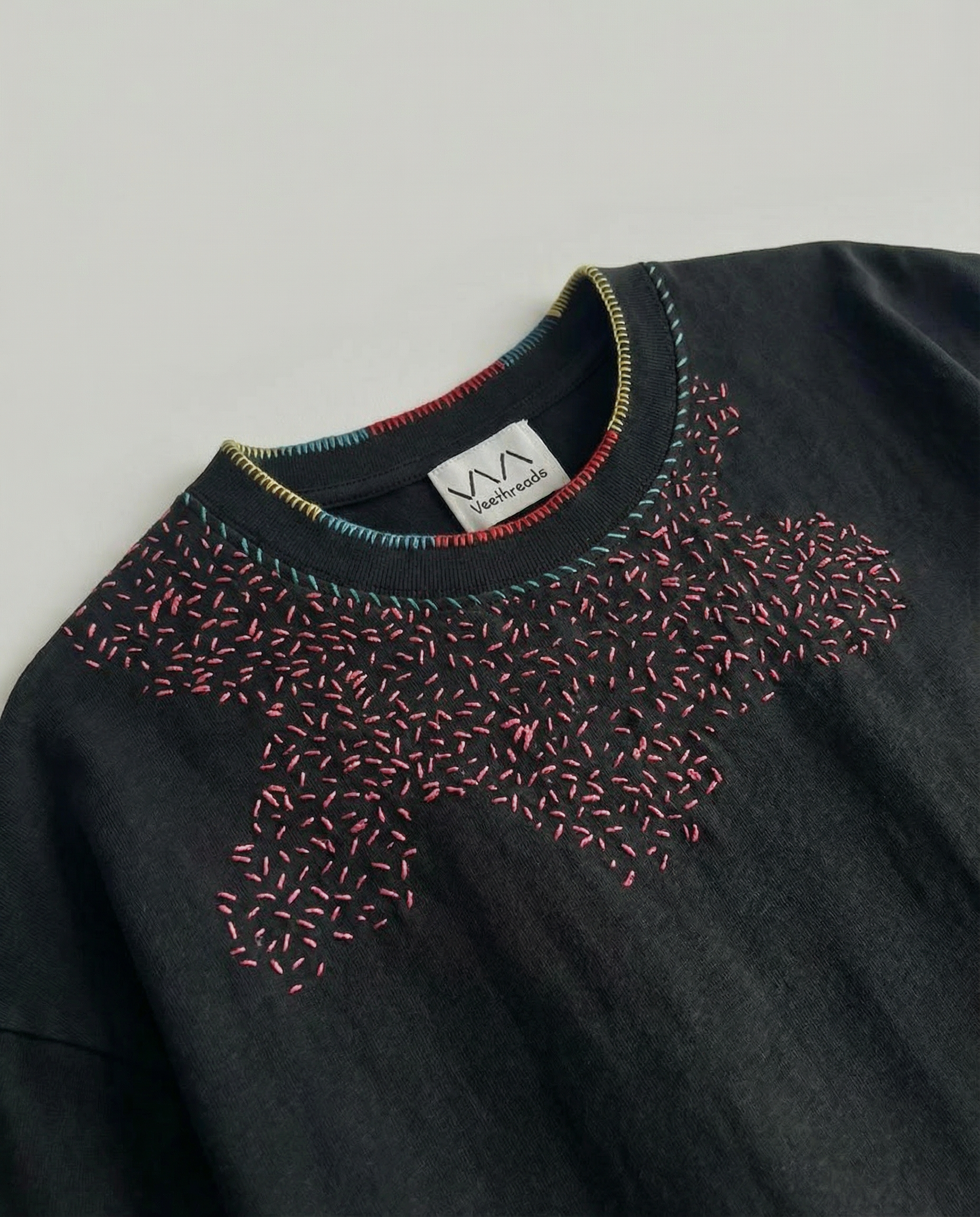 Black sweater with colorful embroidered neckline on a gray background