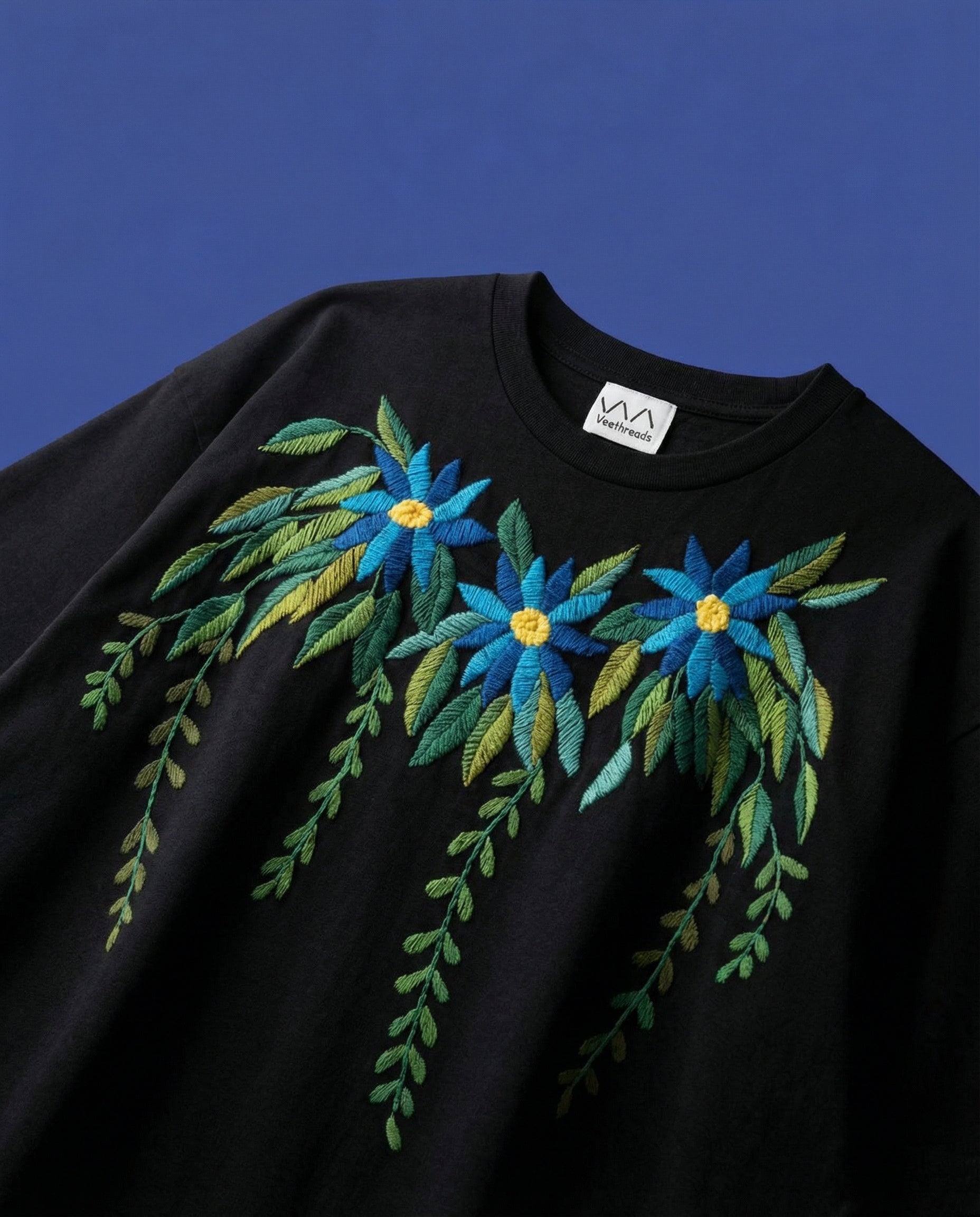 Black t-shirt with blue hand embroidery on a blue background
