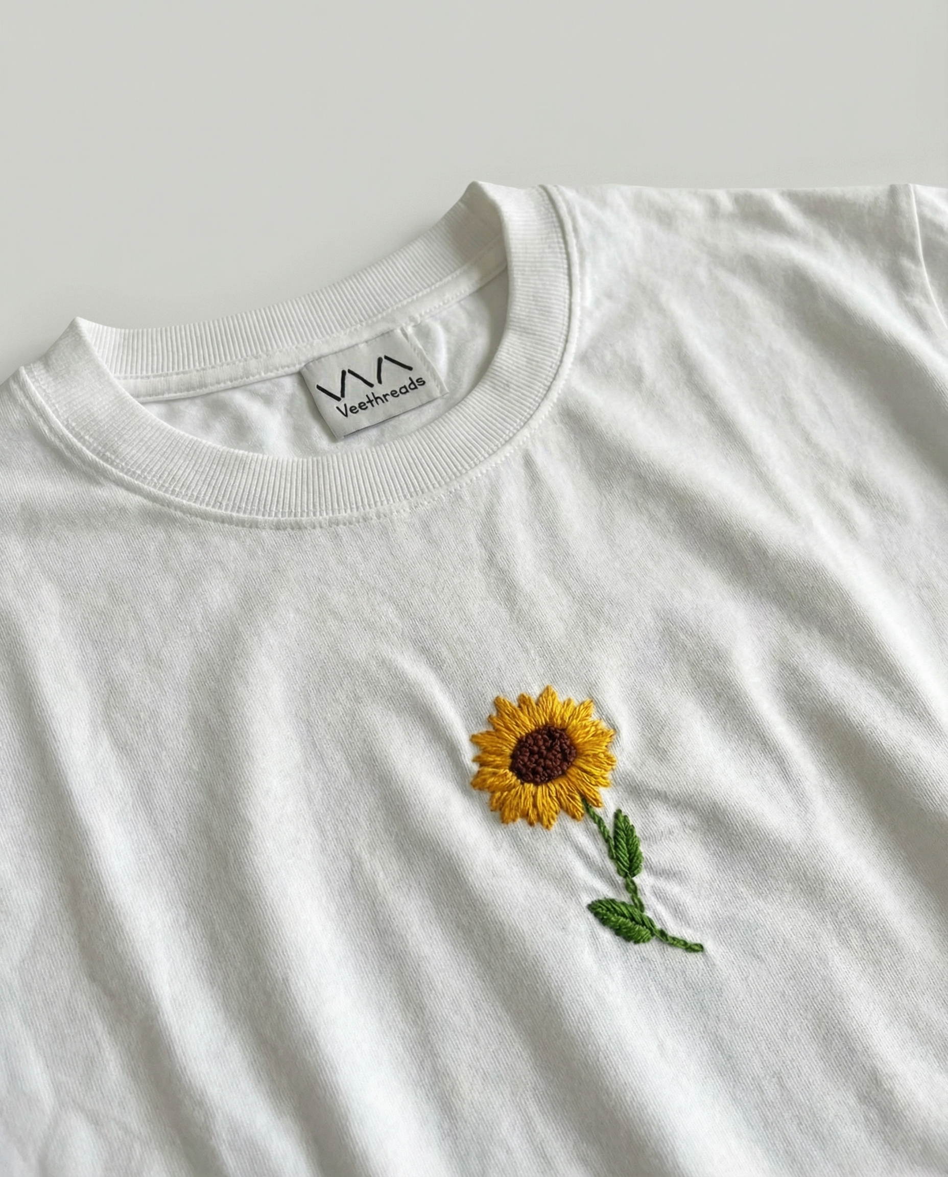 White t-shirt with embroidered sunflower design on a light gray background
