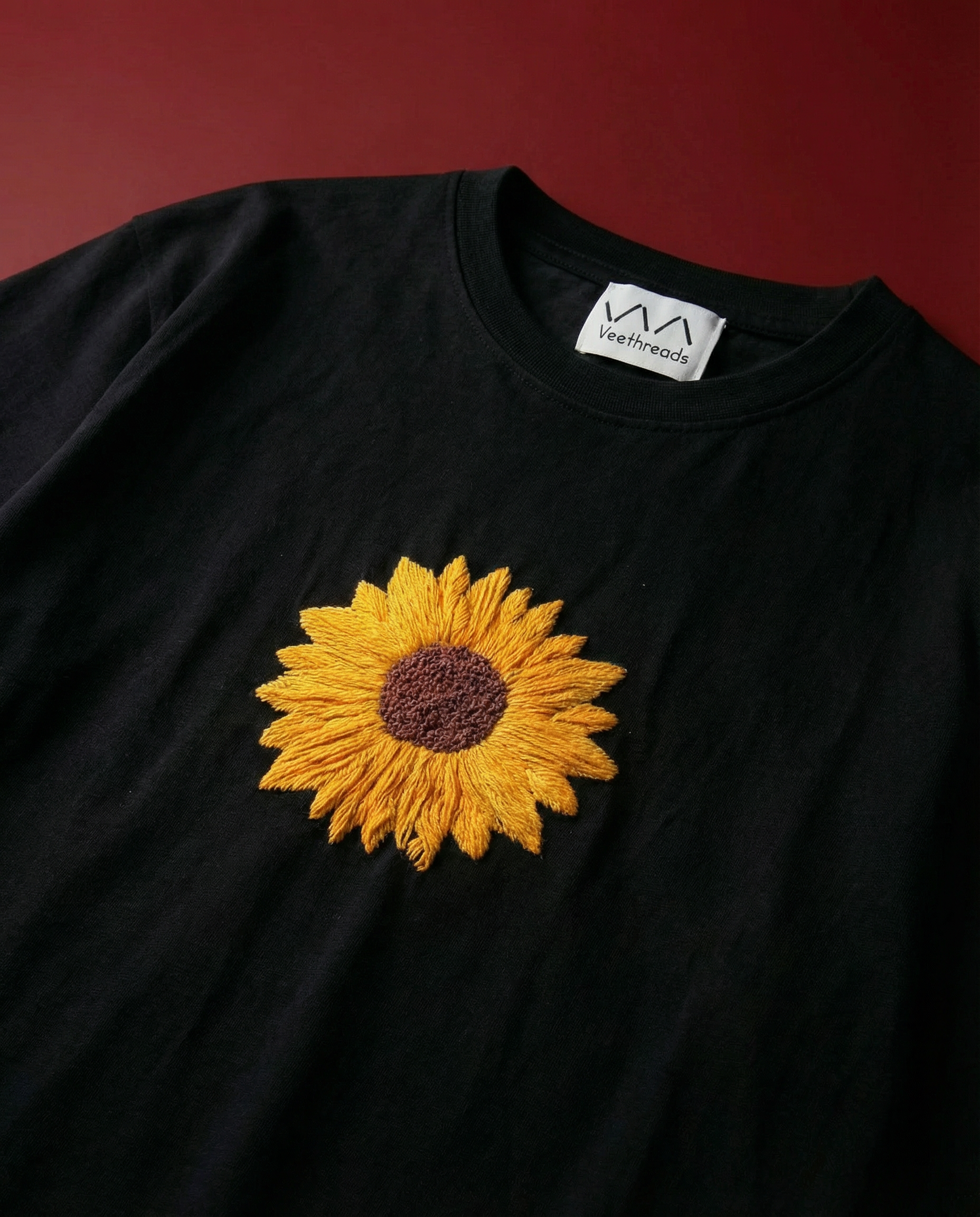 Black t-shirt with a yellow sunflower embroidered design on a red background