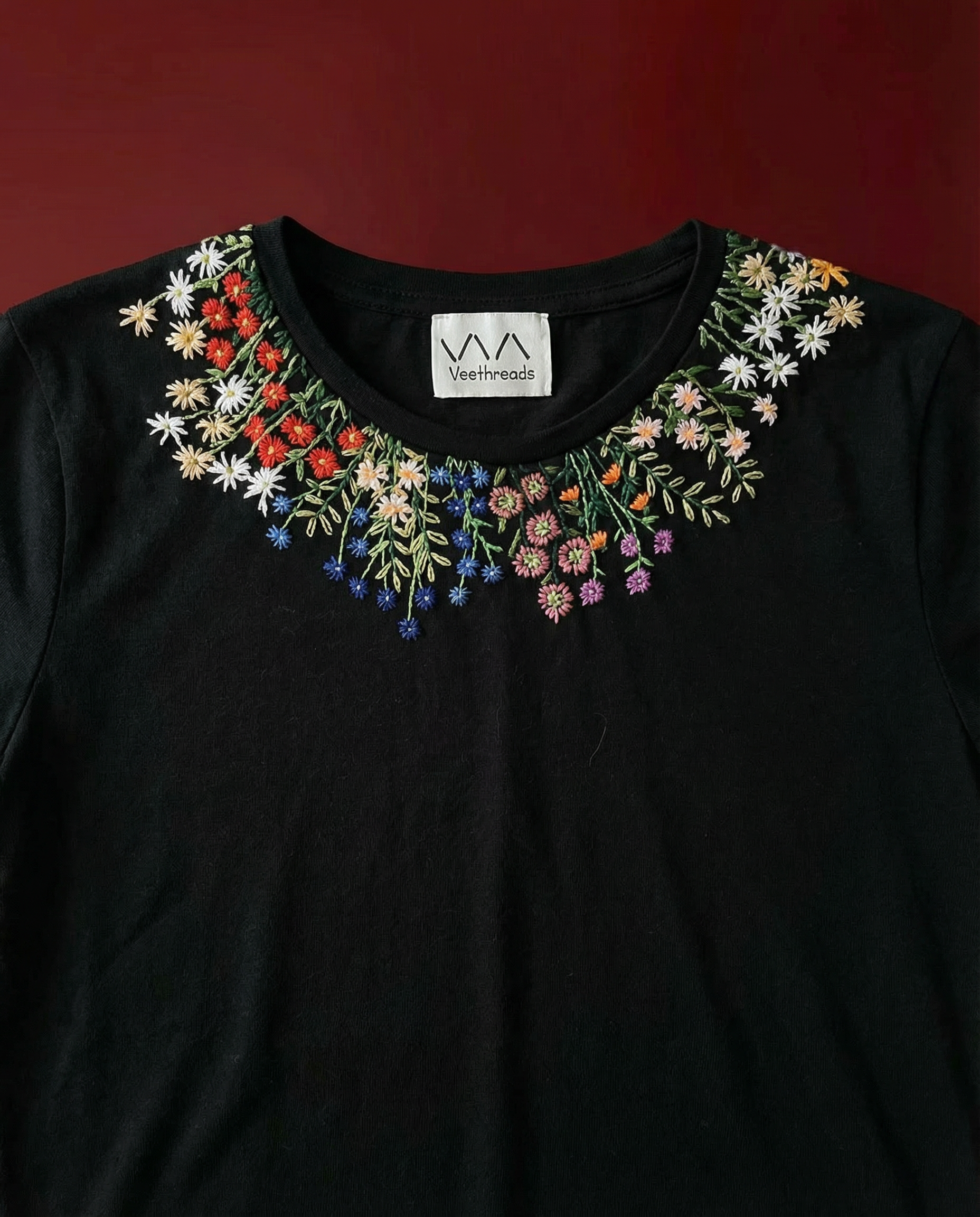 Black shirt with colorful floral embroidery on a dark red background