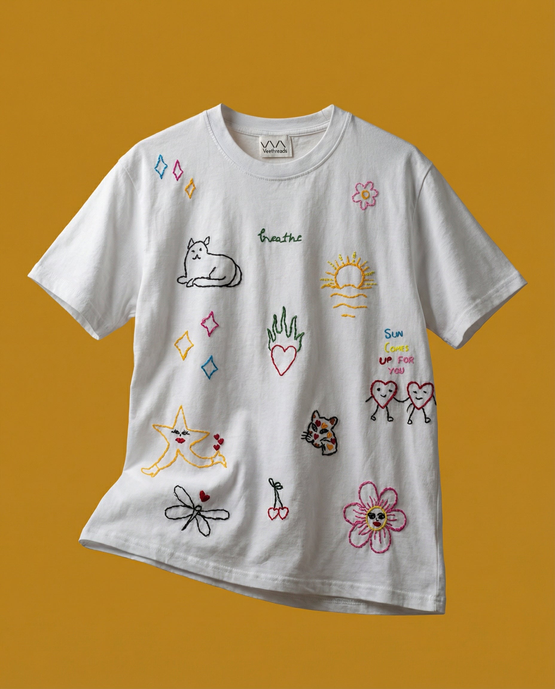 Whimsical doodle embroidered t-shirt — white cotton tee with colourful hand-drawn doodle designs on mustard yellow background