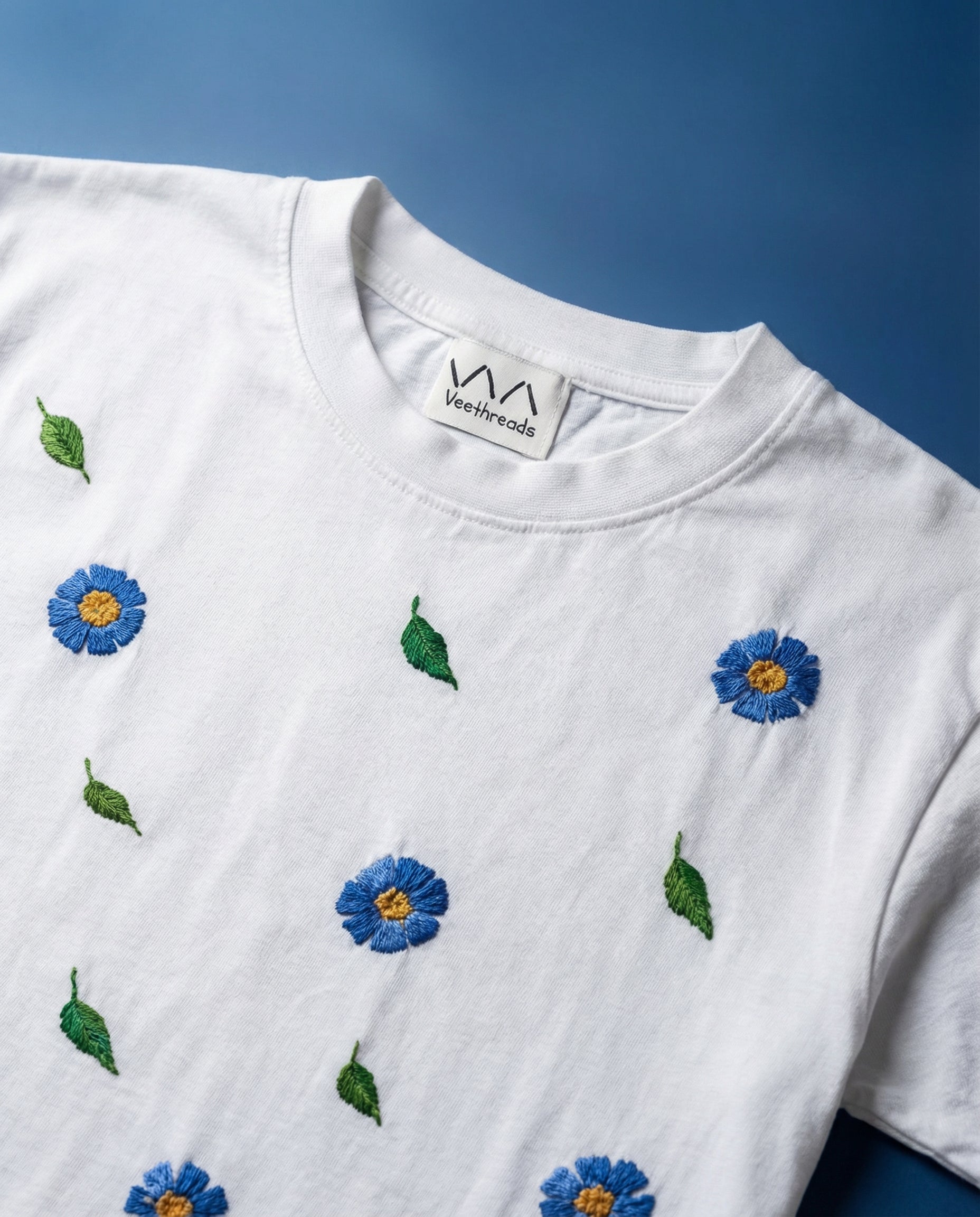 Floral embroidery designs blue — white cotton tee with blue floral hand embroidery on blue background, premium 220 GSM