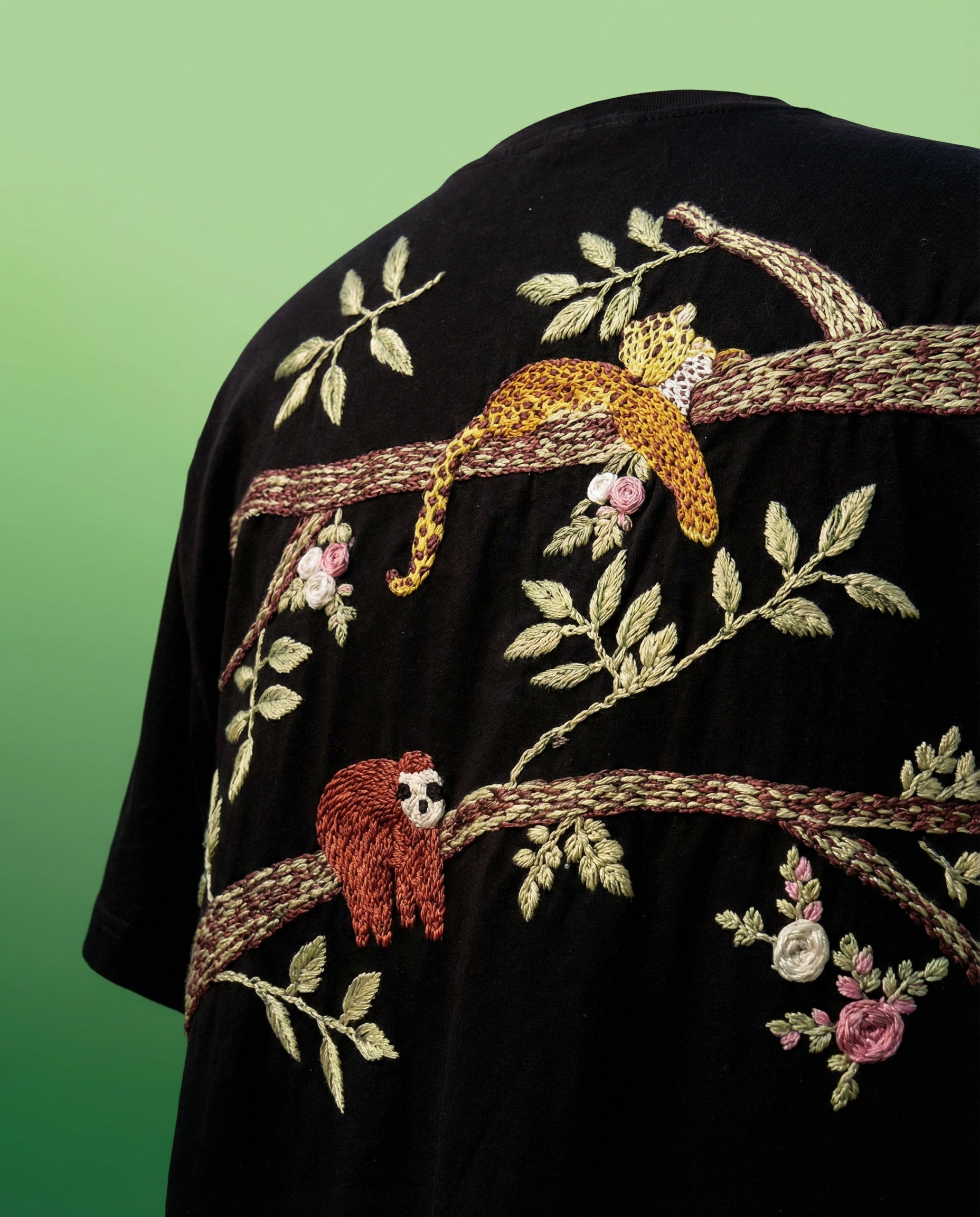 Black shirt with embroidered leopards and sloths on a green background