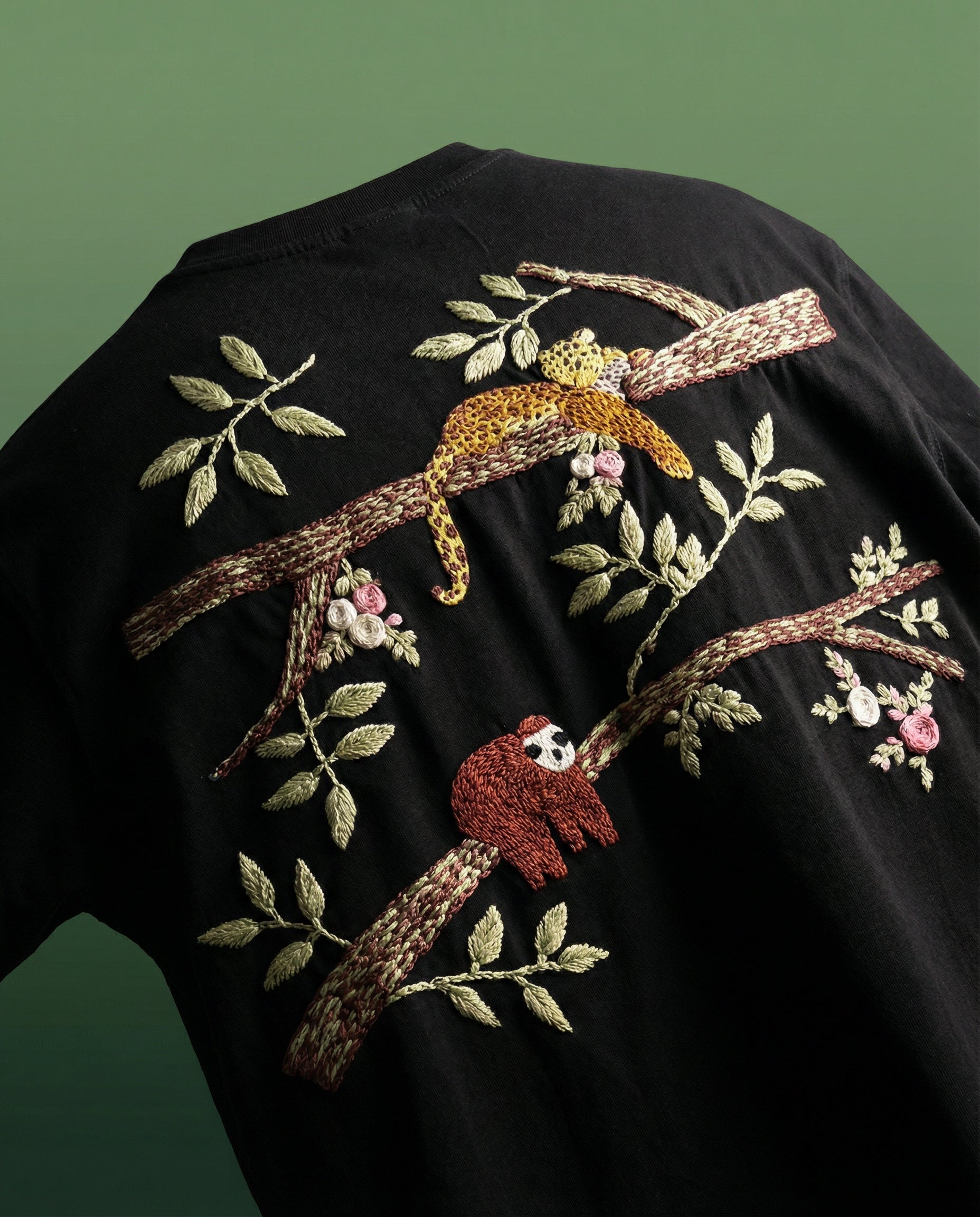 Black shirt with embroidered sloths on branches and leaves.