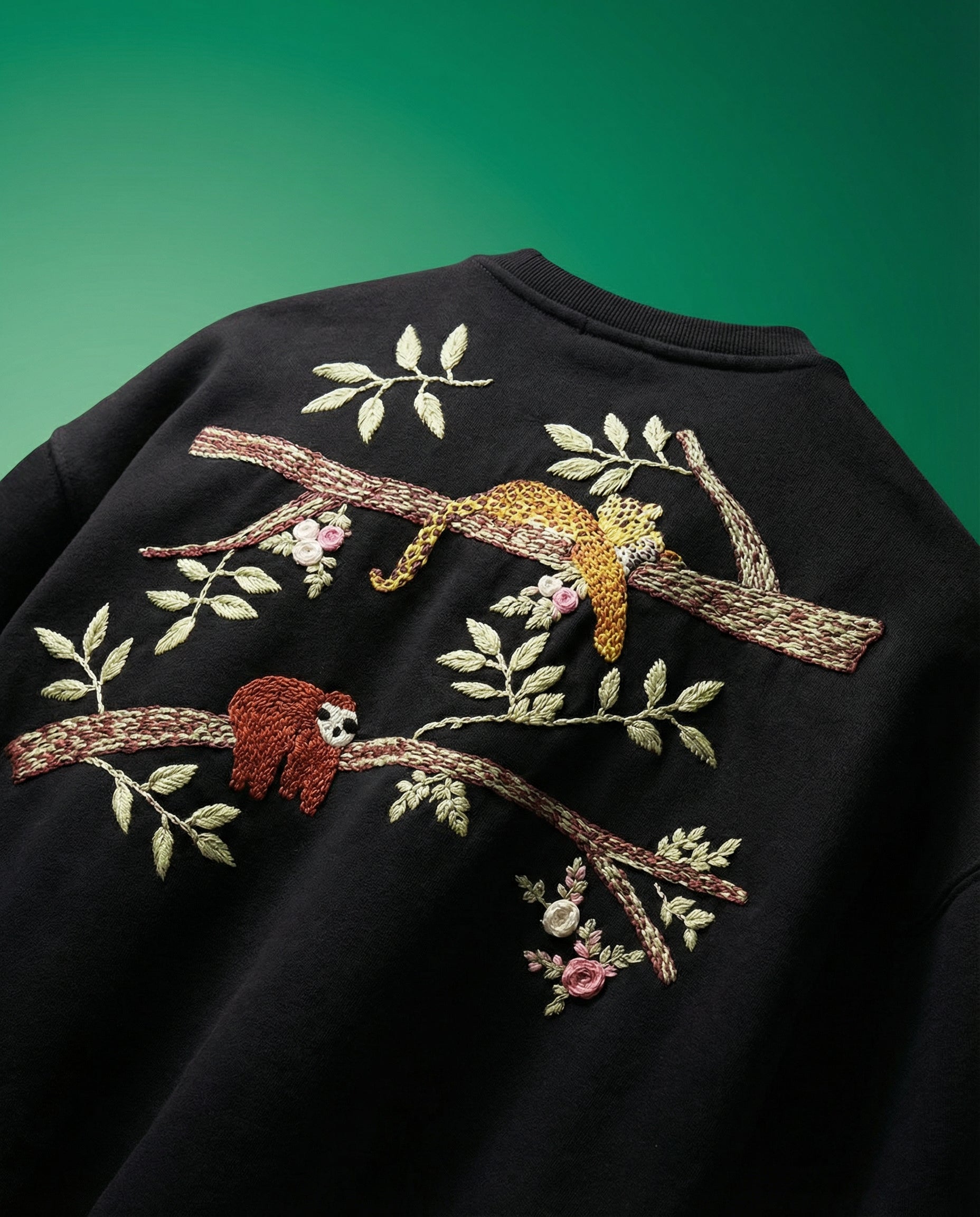 Black tshirt with embroidered sloth and branch design on a green background
