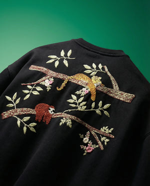 Black tshirt with embroidered sloth and branch design on a green background
