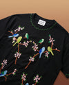 Black t-shirt with colorful bird and floral embroidery on a brown background