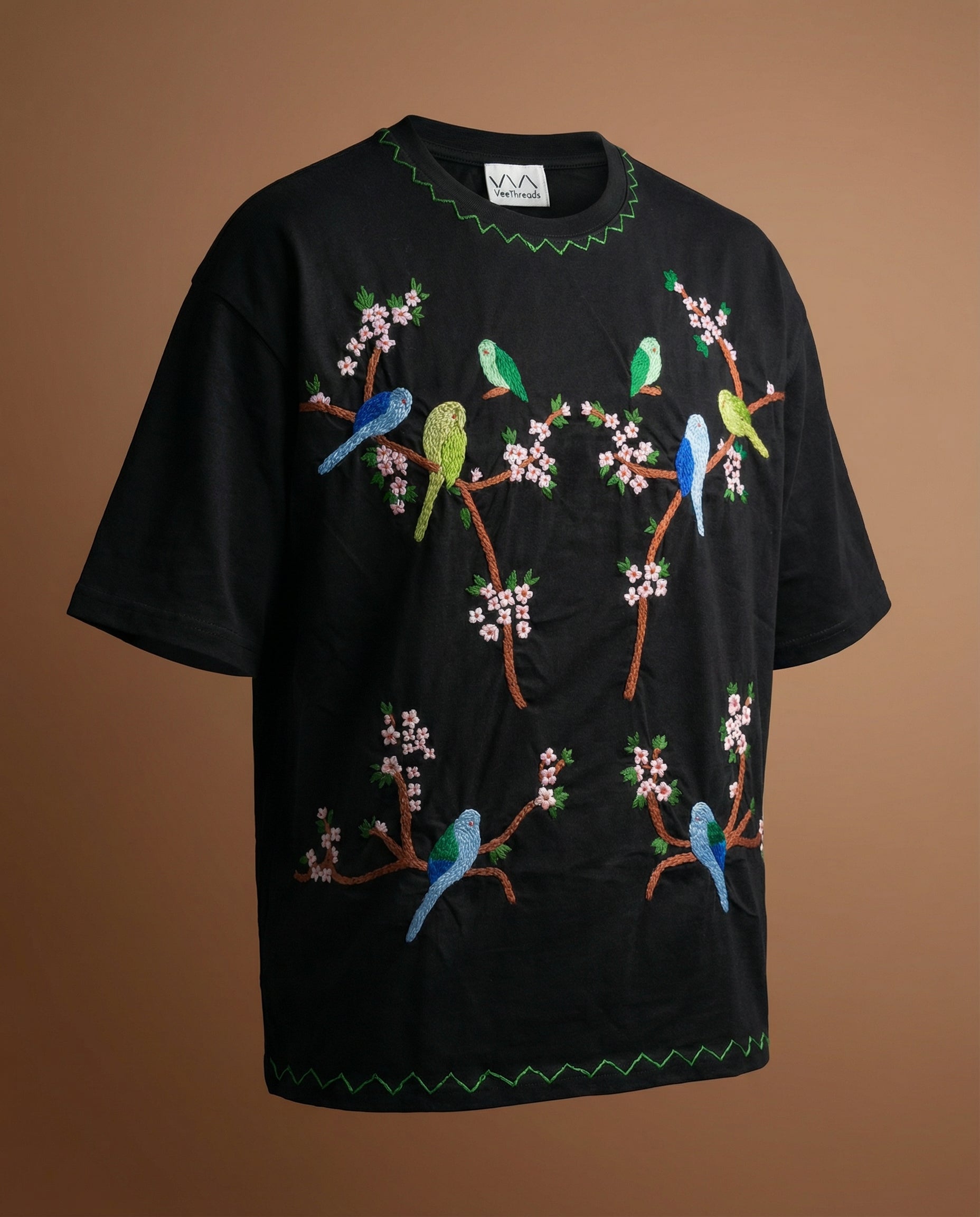 Black t-shirt with colorful bird and floral embroidery on a brown background