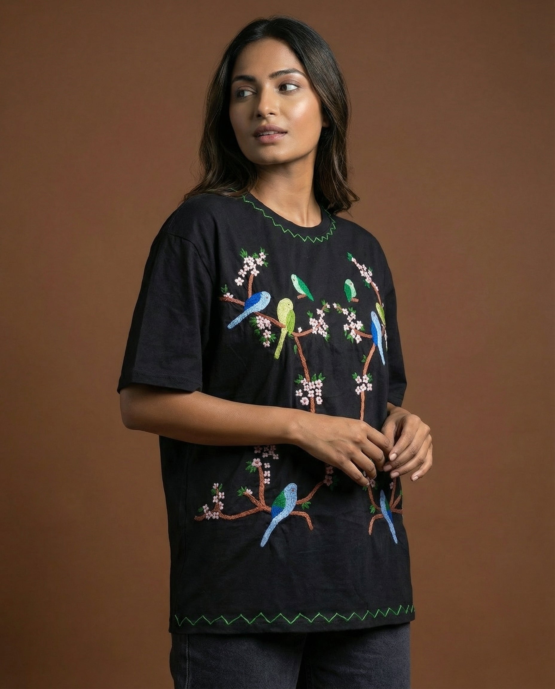 Woman wearing a black t-shirt with colorful bird embroidery against a brown background