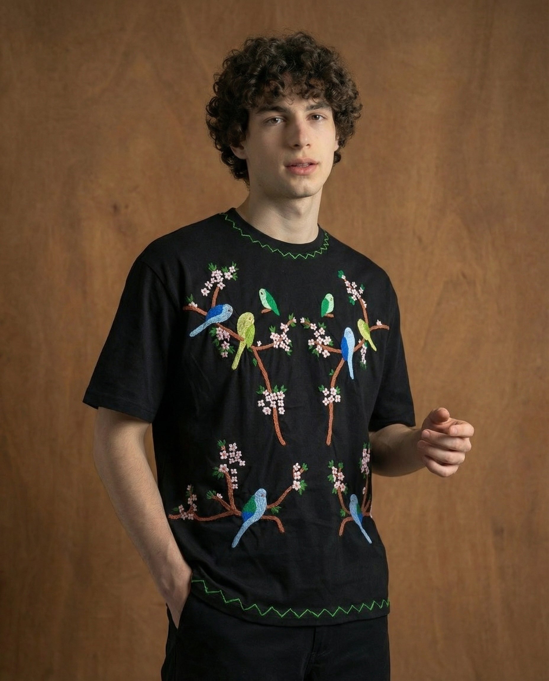 Person wearing a black t-shirt with colorful bird designs on a wooden background