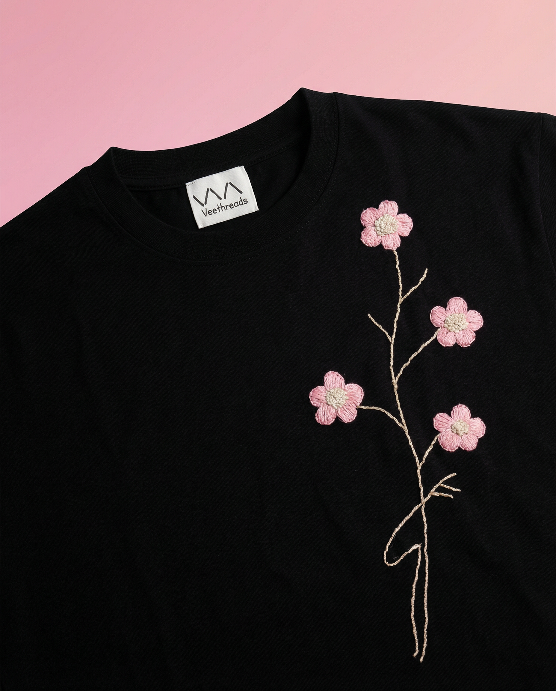 Black t-shirt with pink floral embroidery on a pink background