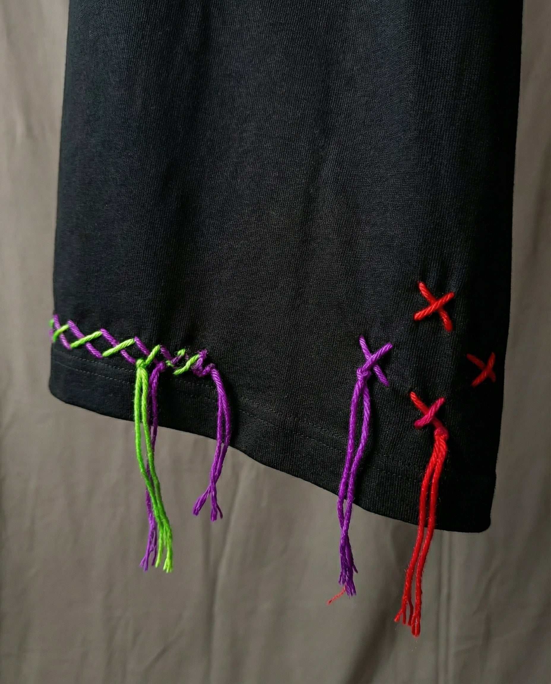 Embroidery designs t shirt kantha — black cotton garment with colourful hand-stitched strings hanging from bottom edge, neutral background