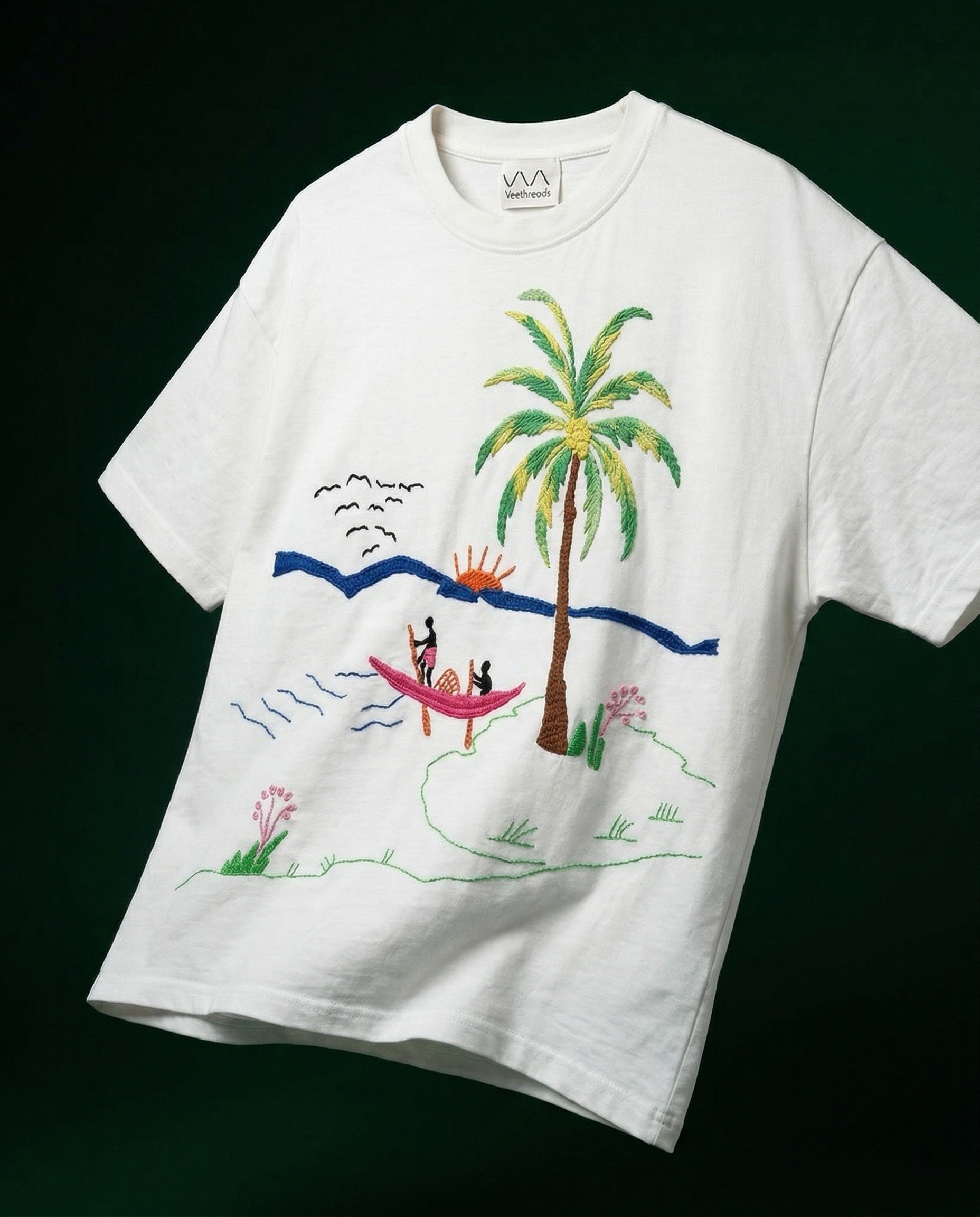 White t-shirt with a colorful embroidery design of a palm tree and beach scene on a black background