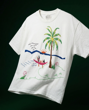 White t-shirt with a colorful embroidery design of a palm tree and beach scene on a black background