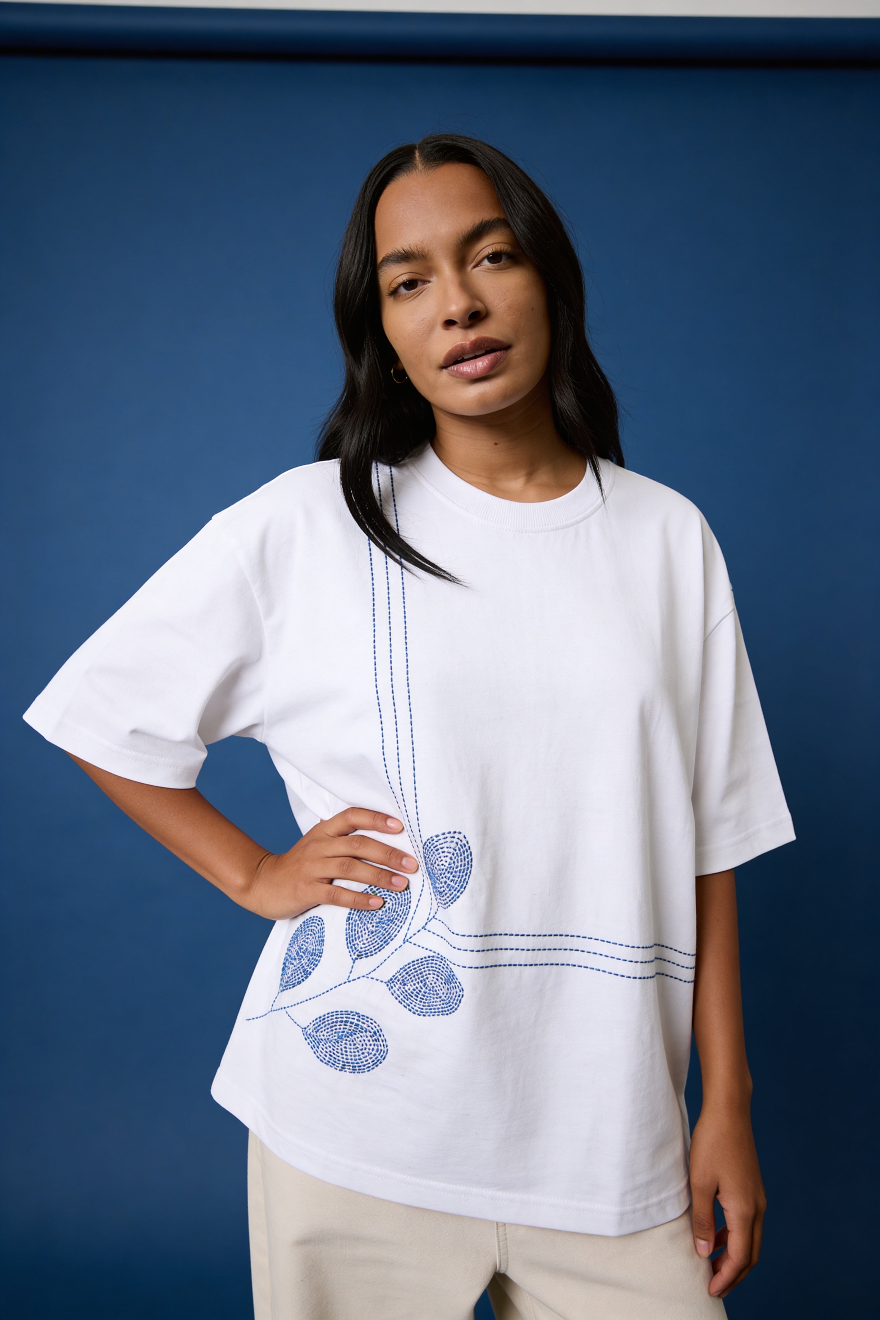 Woman wearing a white t-shirt with blue floral embroidery against a blue background