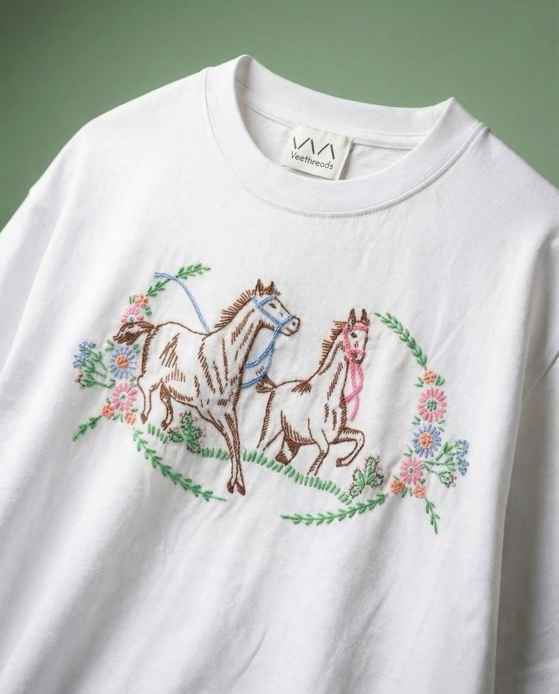 White t-shirt with embroidered horses and floral designs on a green background