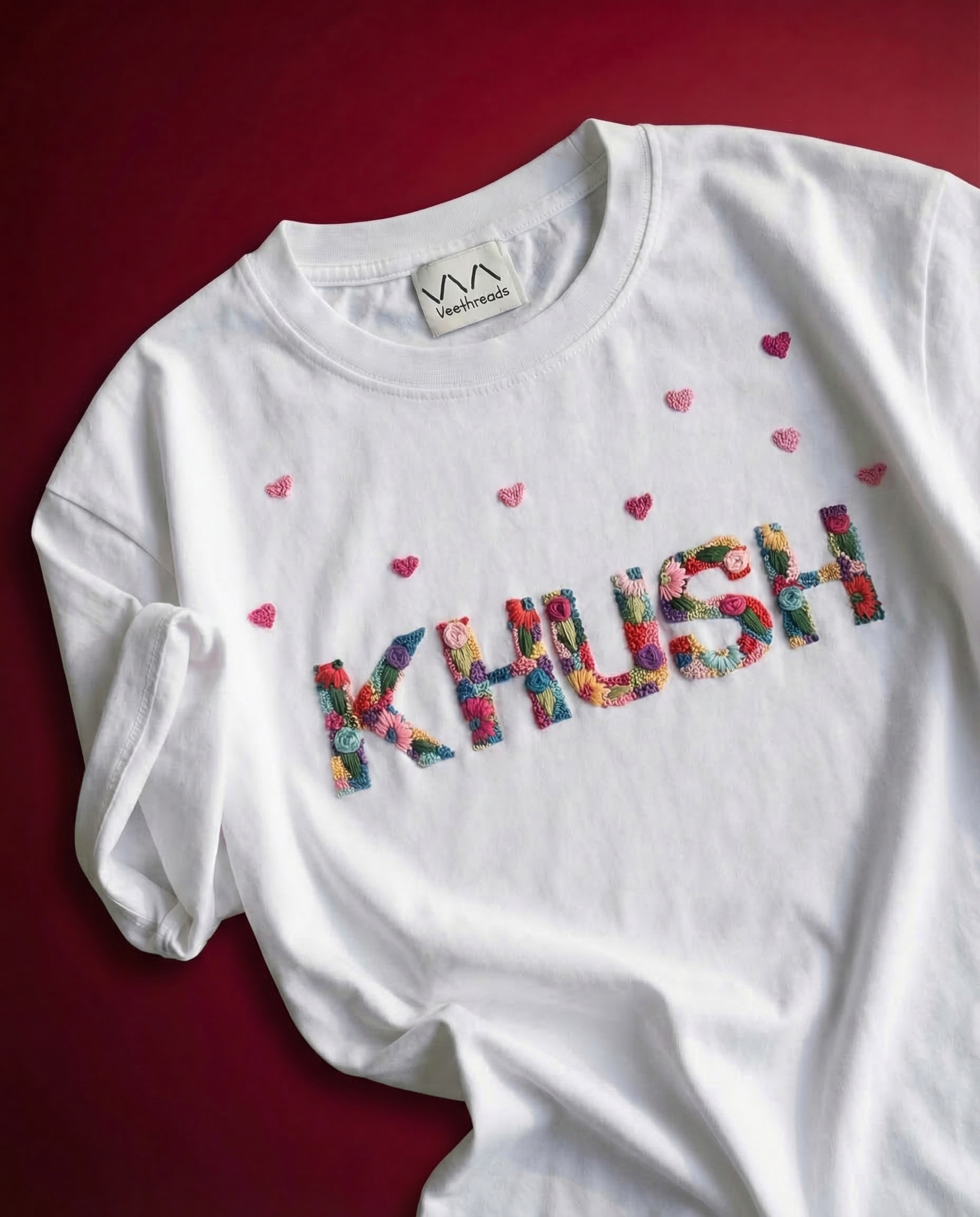 Custom embroidery sweatshirt with name — white sweatshirt with colourful 'KHUSH' text and hand-embroidered hearts on red background