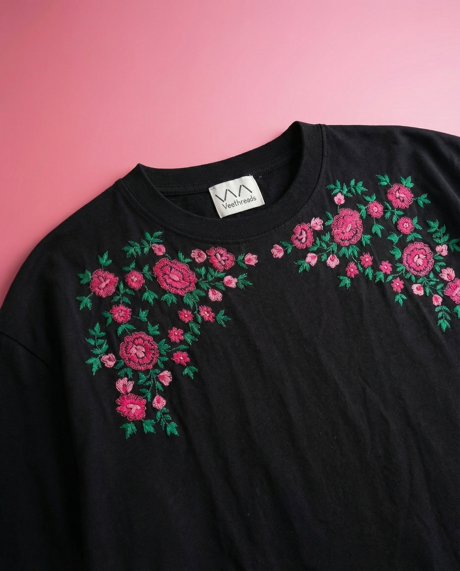 Black t-shirt with pink floral embroidery on a pink background