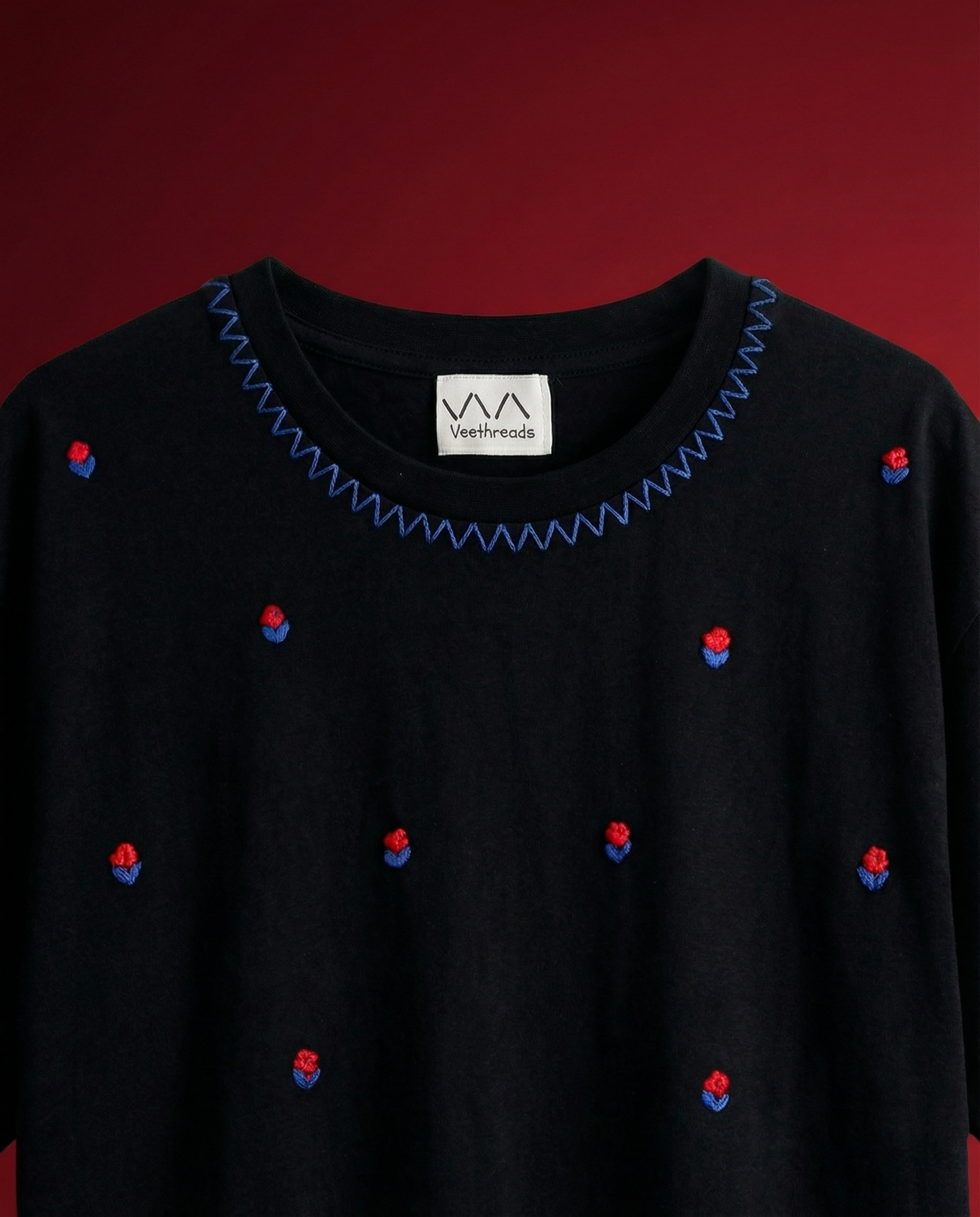 Black sweater with blue and red embellishments on a red background