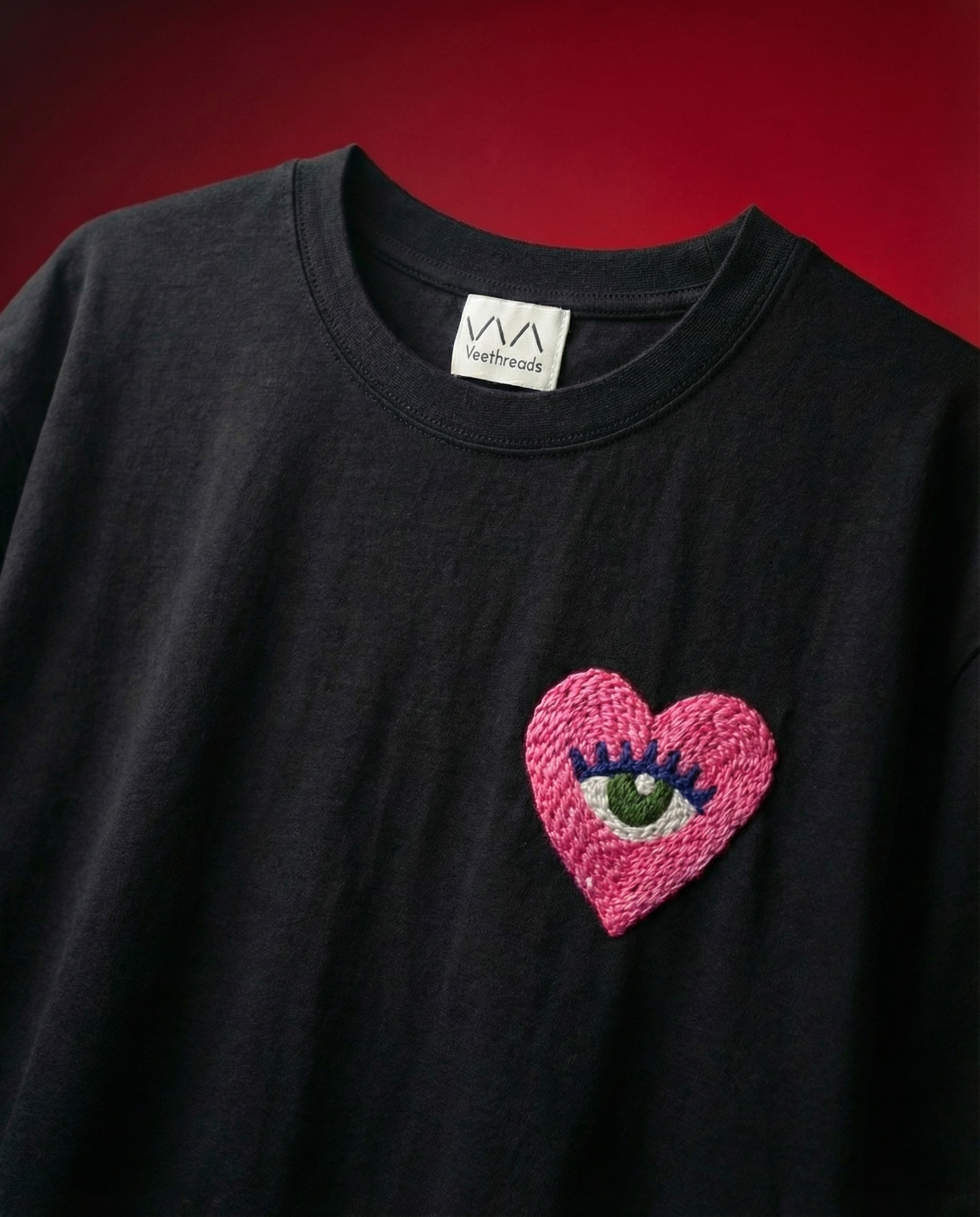 Black t-shirt with a pink heart design featuring a eye on a red background
