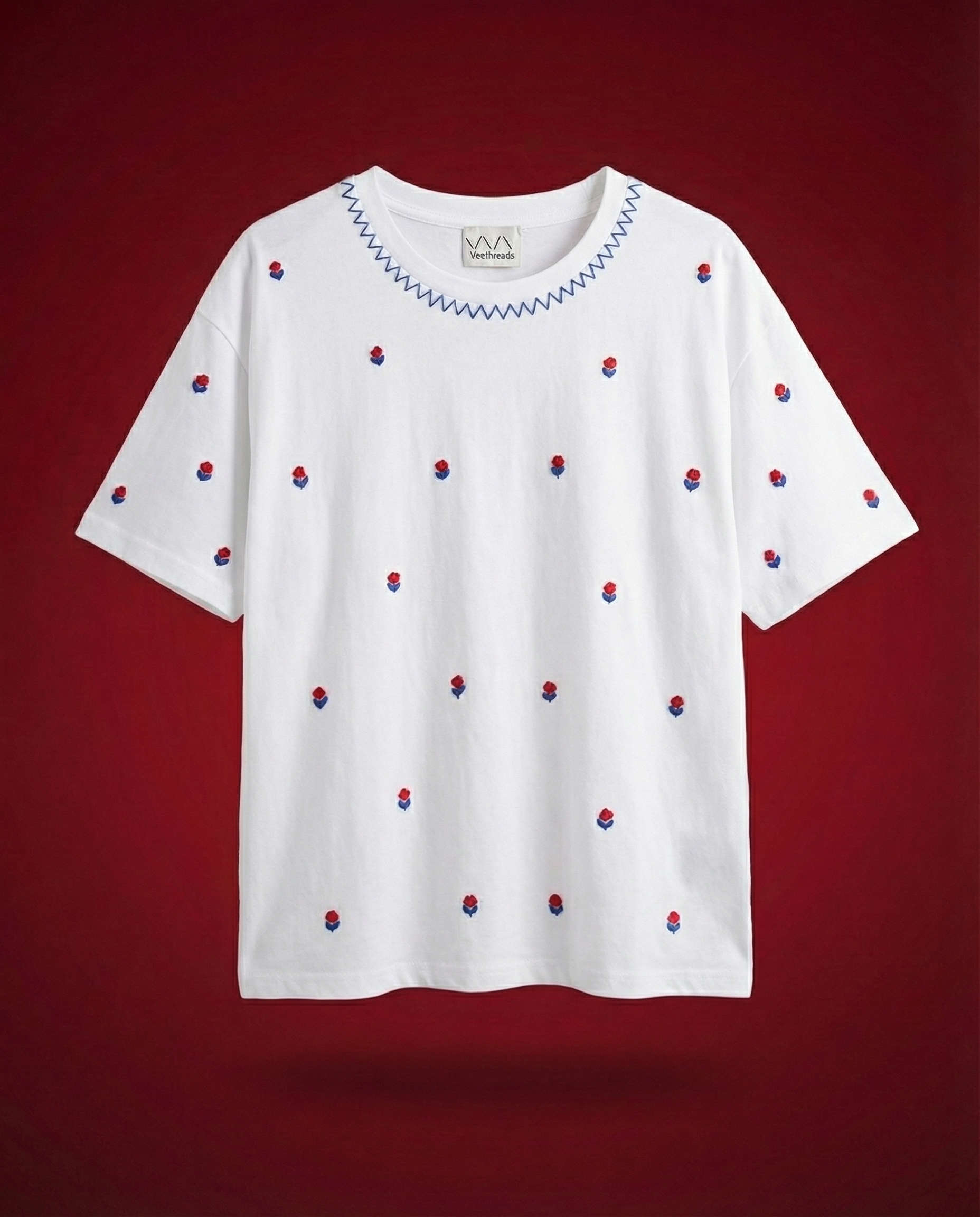 White t-shirt with red and blue floral embroidery on a red background