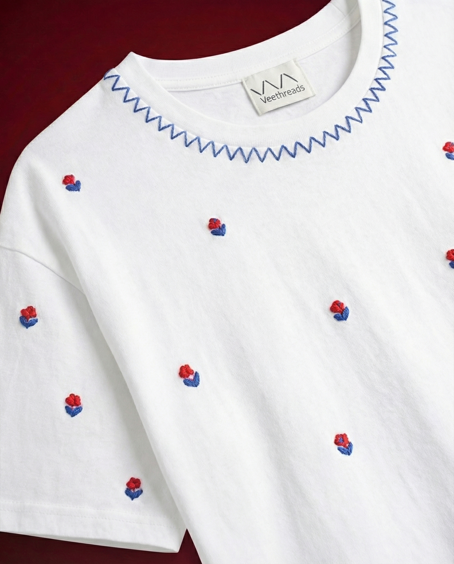 Close up of hand embroidered red rose buds and blue chevron zigzag neckline stitch on Cherry Blossom black tee by Veethreads