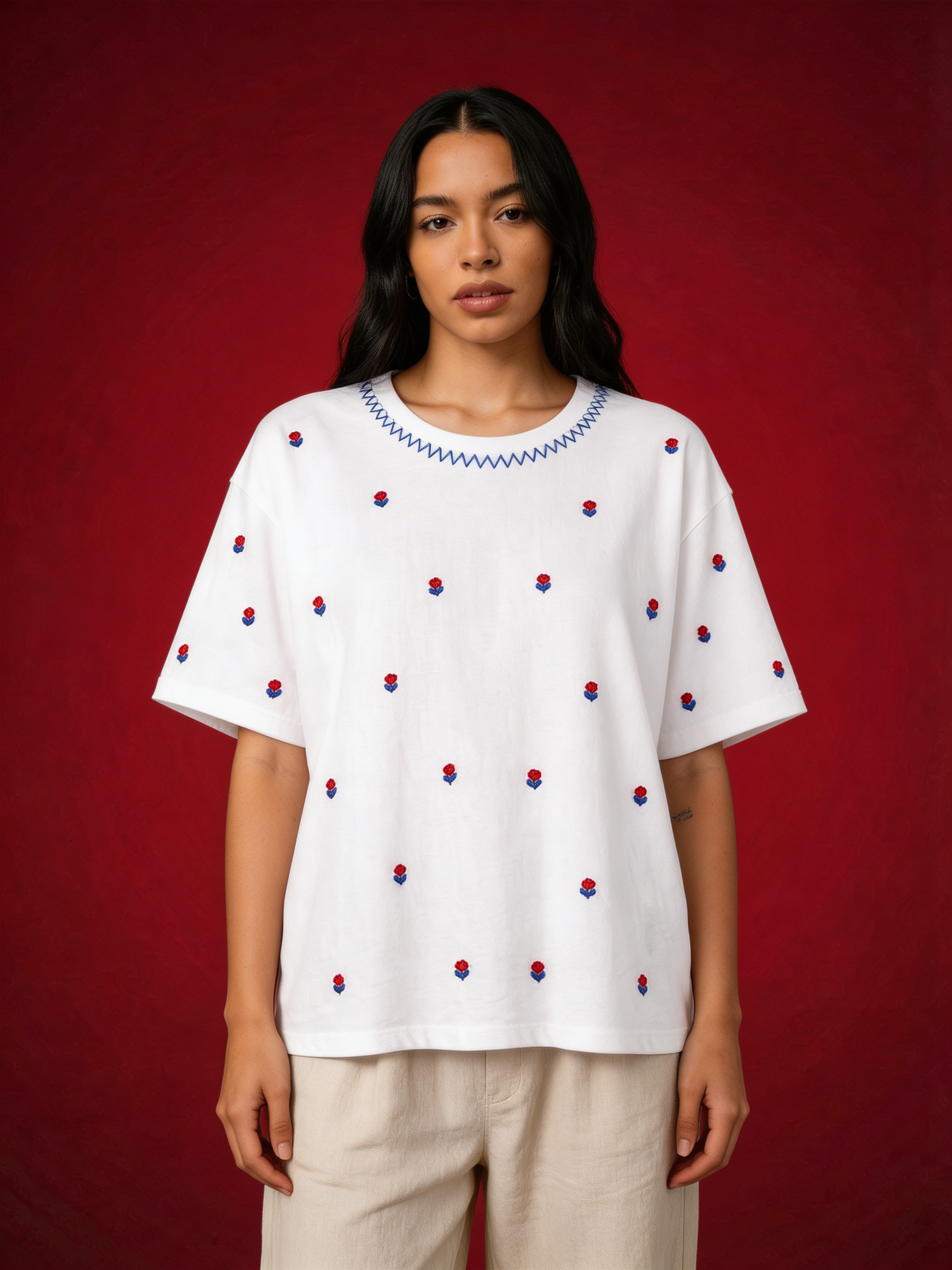 Woman wearing a white blouse with red and blue embroidery against a red background