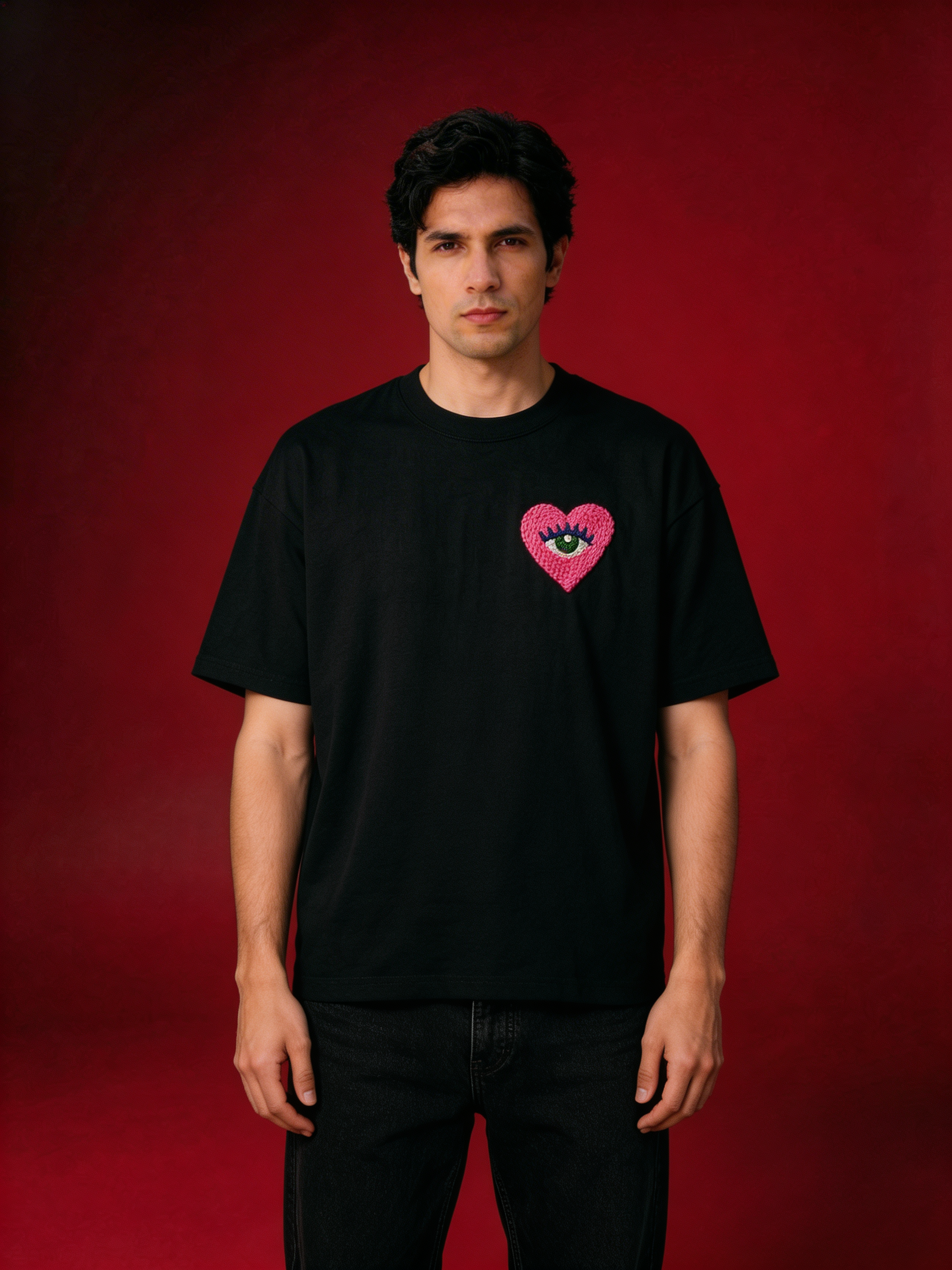 Surreal Love Eye embroidery — a pink heart with a green eye hand-stitched on a black 220 GSM cotton tee, made by women artisans in India.