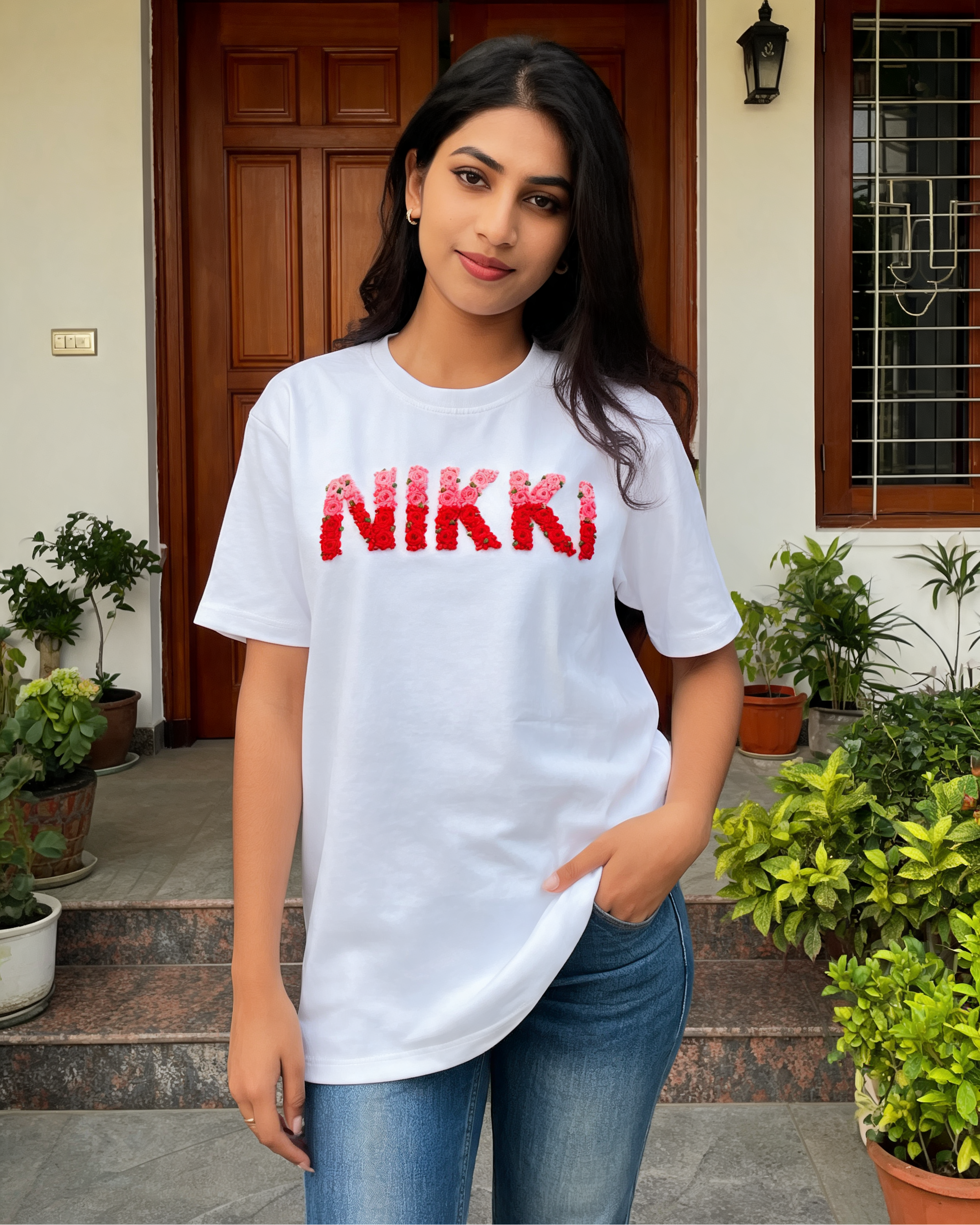 Woman wearing a white t-shirt with 'NIKKI' custom name embroidered in red, standing outdoors.
