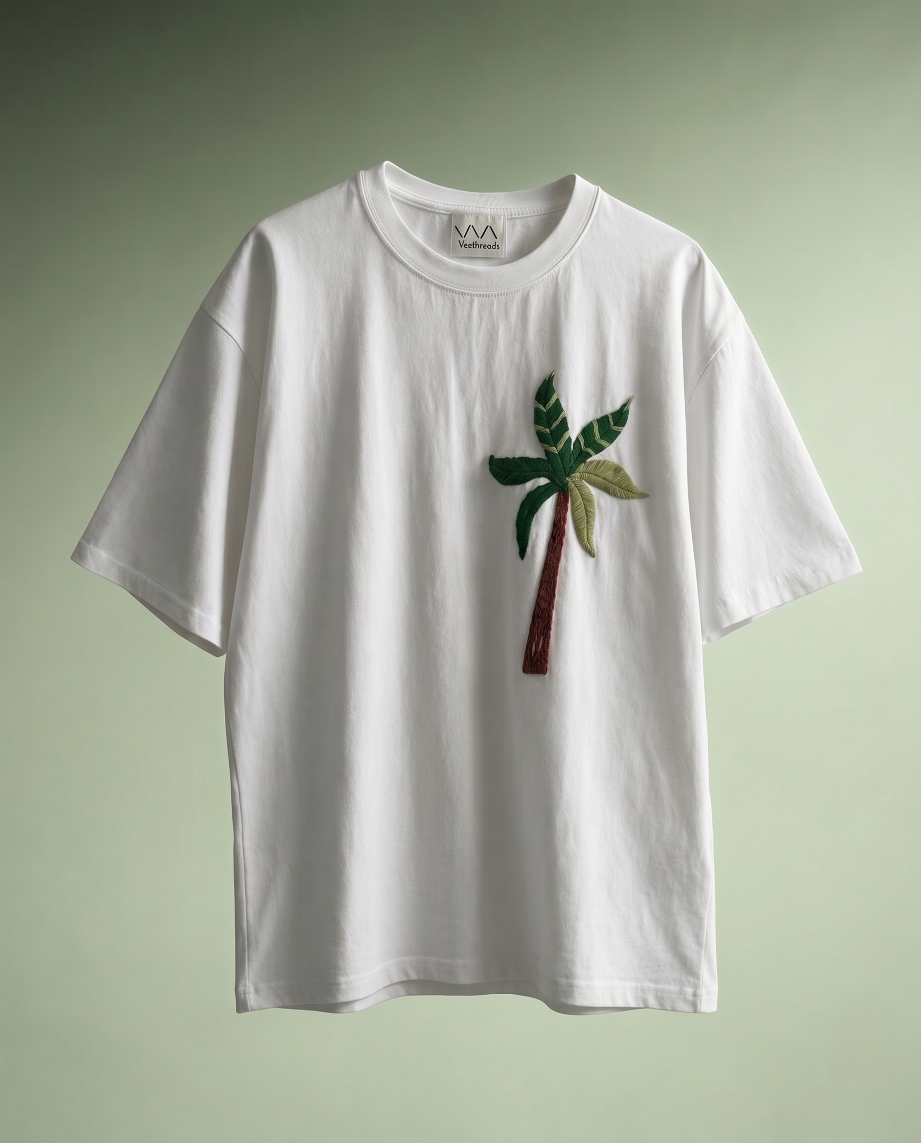 Coastal embroidery designs for shirts — close-up of hand-embroidered palm tree fronds on cotton tee, multi-shade green thread