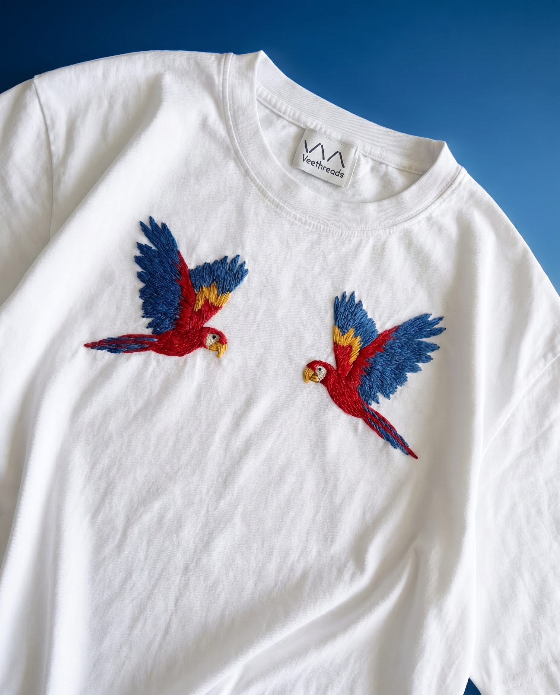 White sweatshirt with embroidered parrot designs on a blue background