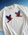 White t-shirt with embroidered parrot designs on a blue background