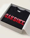 Black t-shirt with red and pink custom name embroidered  'SAKSHEE' in a box on a light background