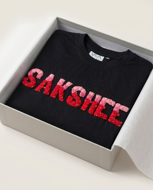 Black t-shirt with red and pink custom name embroidered  'SAKSHEE' in a box on a light background