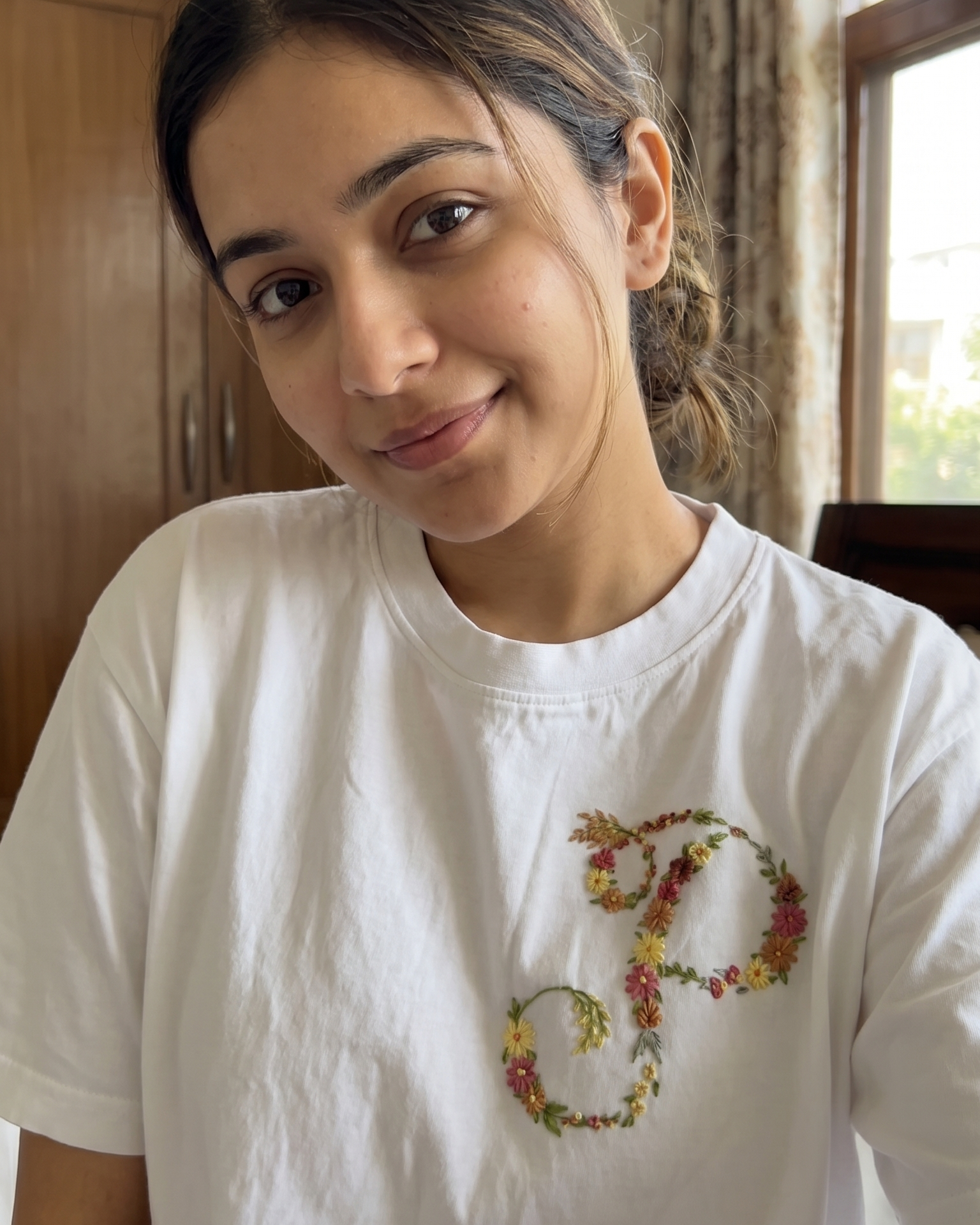 Person wearing a white t-shirt with a colorful customised name embroidered design in a room.