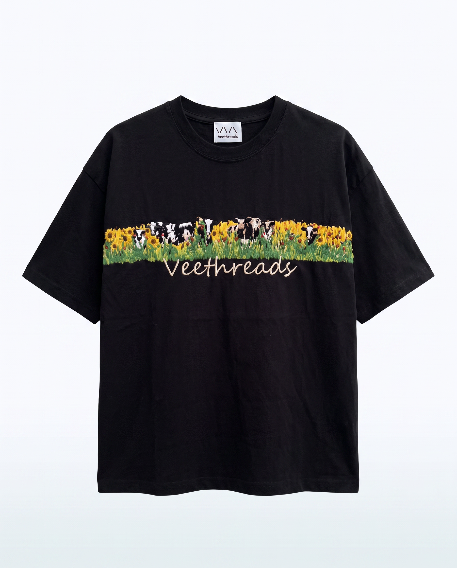 Black hand embroidered oversized t-shirt with grazing cows and sunflower meadow stitched across the chest