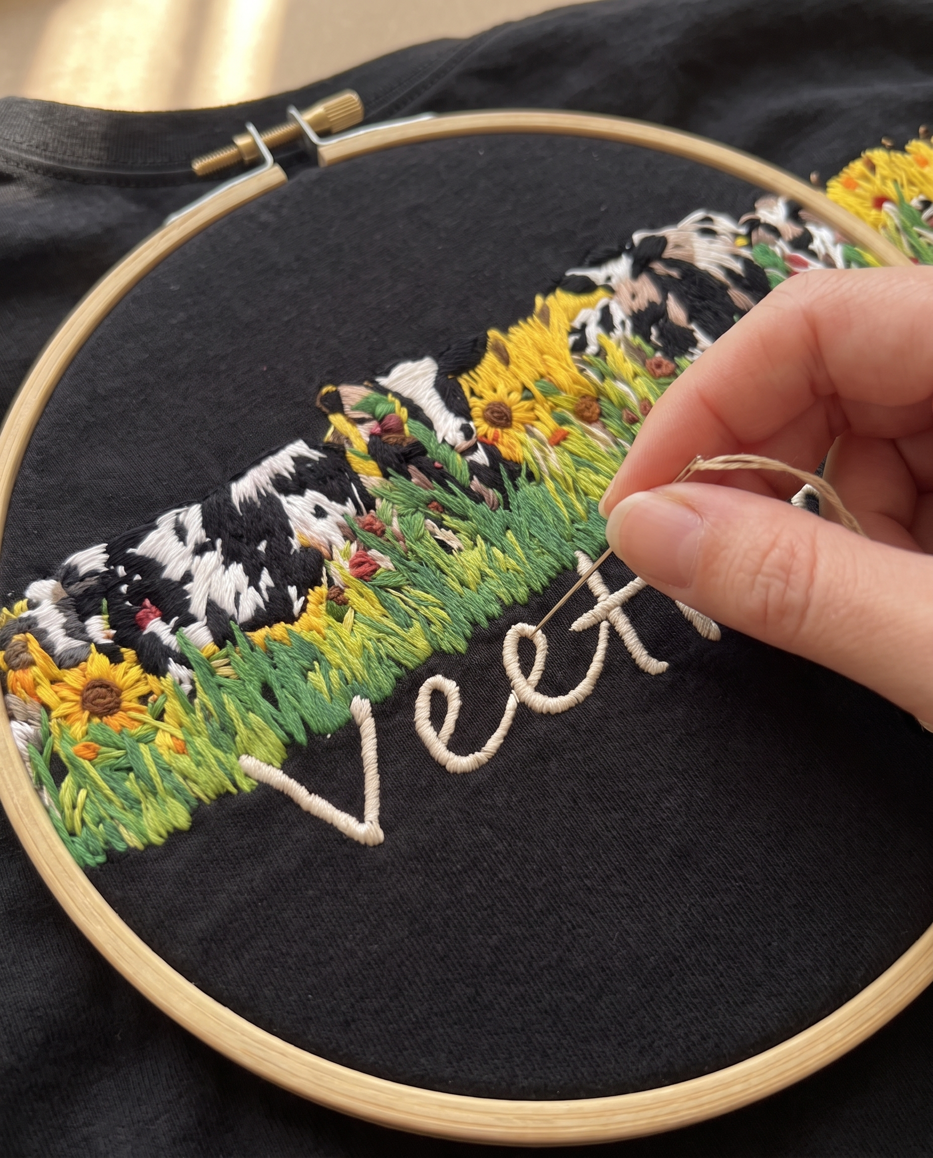Hand embroidering the Veethreads meadow design on black cotton in a wooden hoop, sunflowers and cows in progress