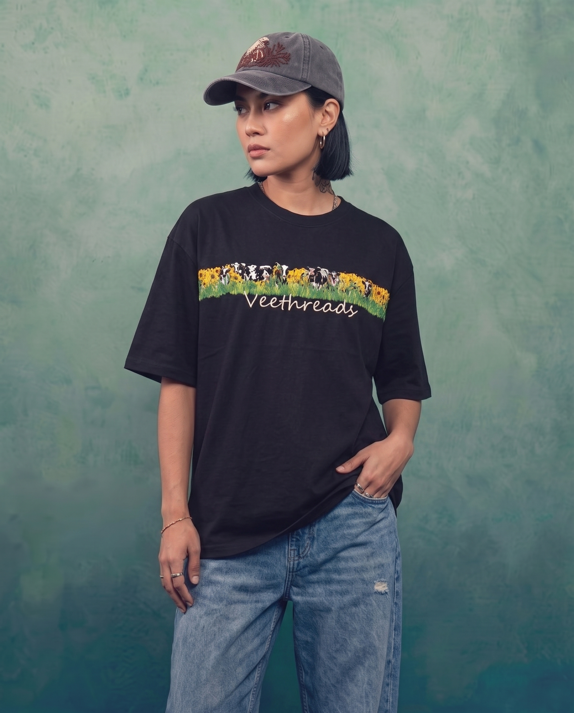 Woman wearing black embroidered oversized t-shirt with hand stitched cow and sunflower band, styled with blue jeans