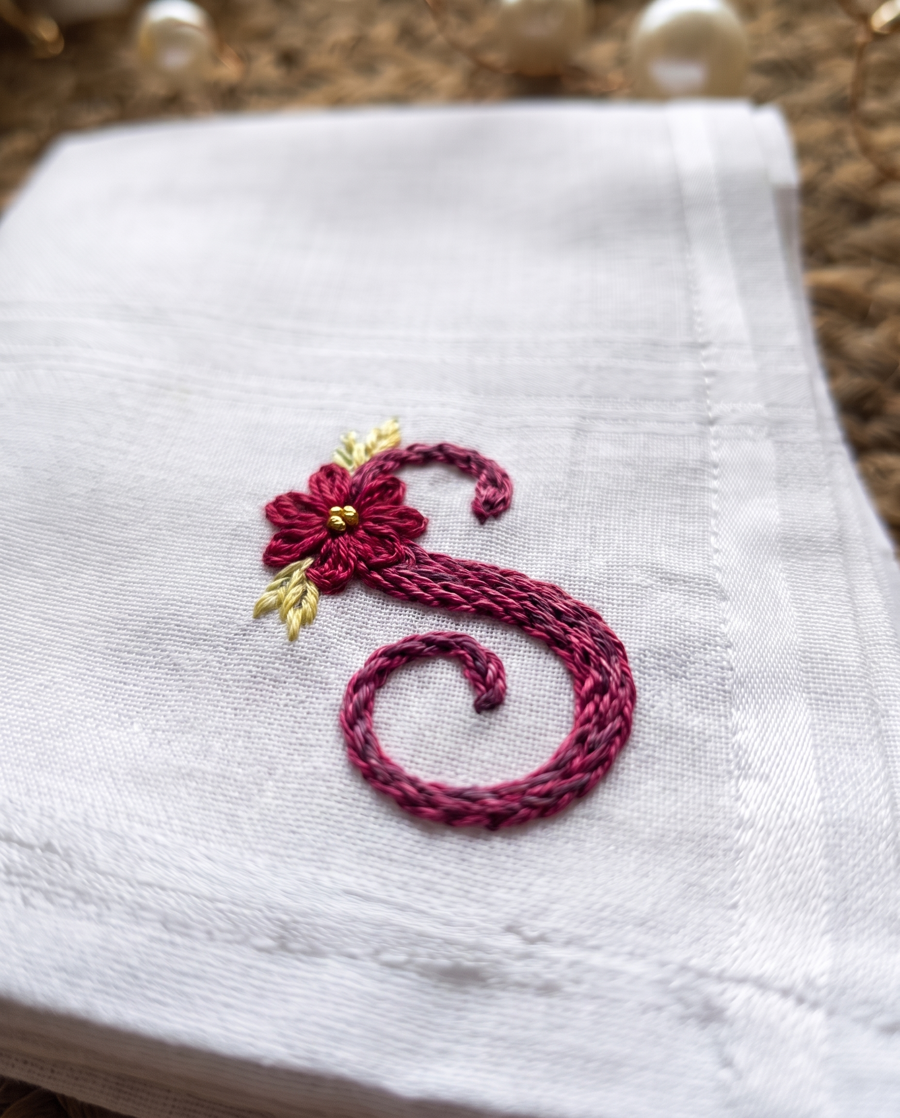 Embroidered handkerchief with the initial S hand stitched in wine thread beside a small flower on white cotton