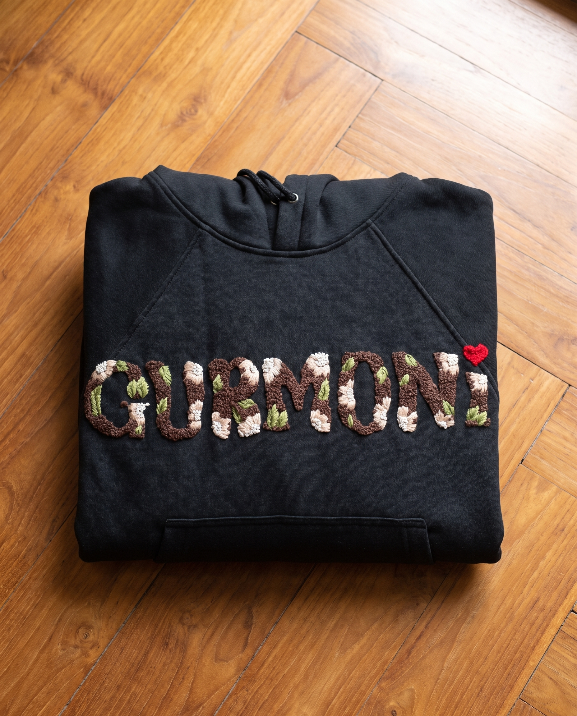 Black embroidered hoodie with the name Gurmoni hand stitched in floral letters and a small red heart