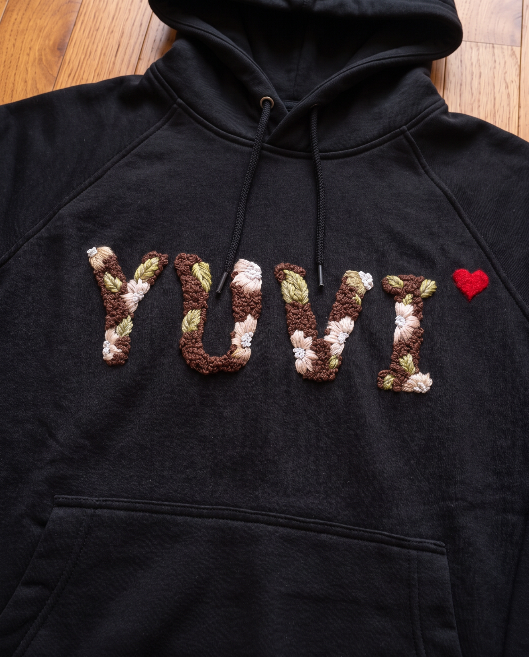 Personalised black hoodie with the name Yuvi embroidered in knotted brown letters and cream daisies
