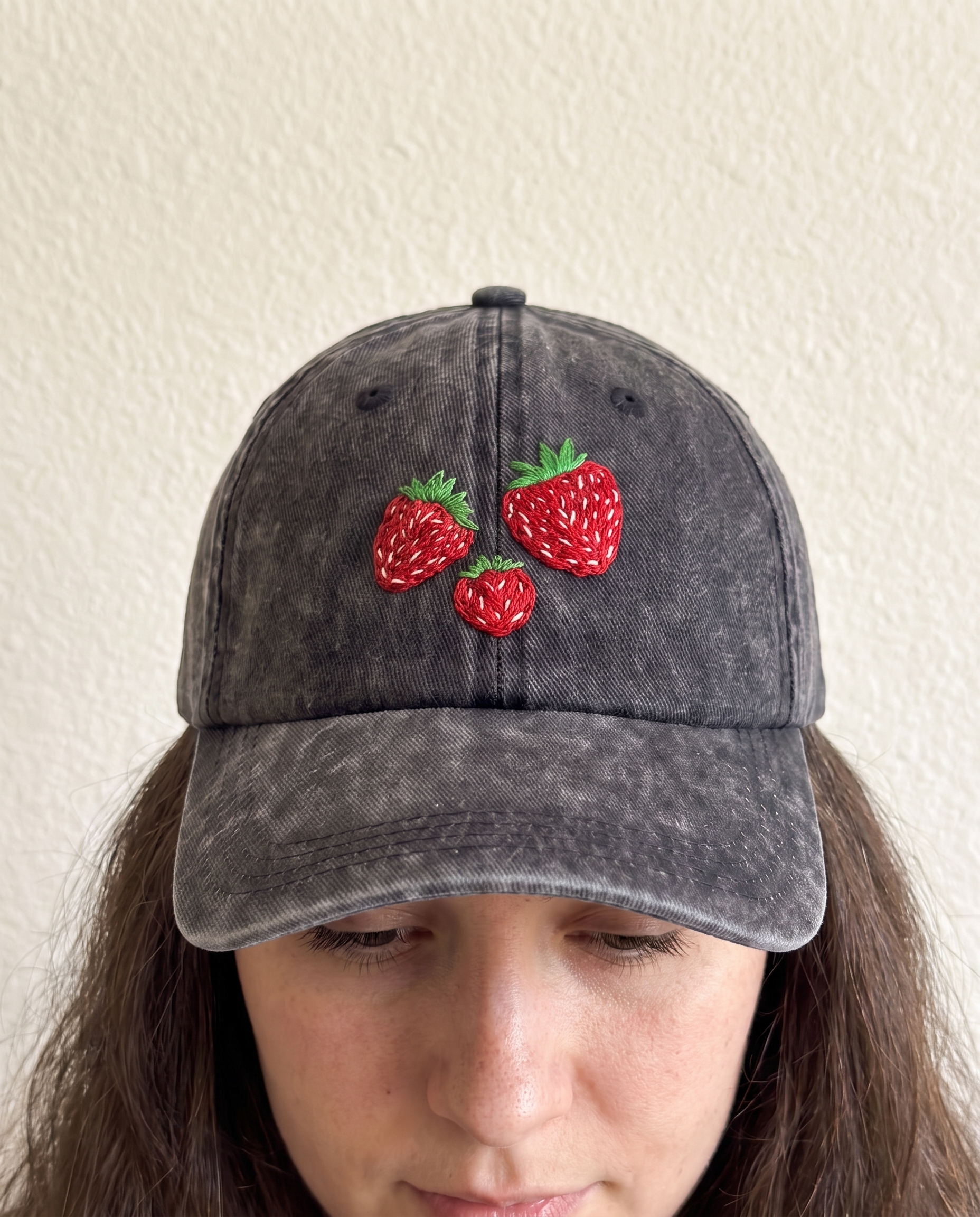Woman wearing the hand-embroidered strawberry cap, head tilted down to show all three berries