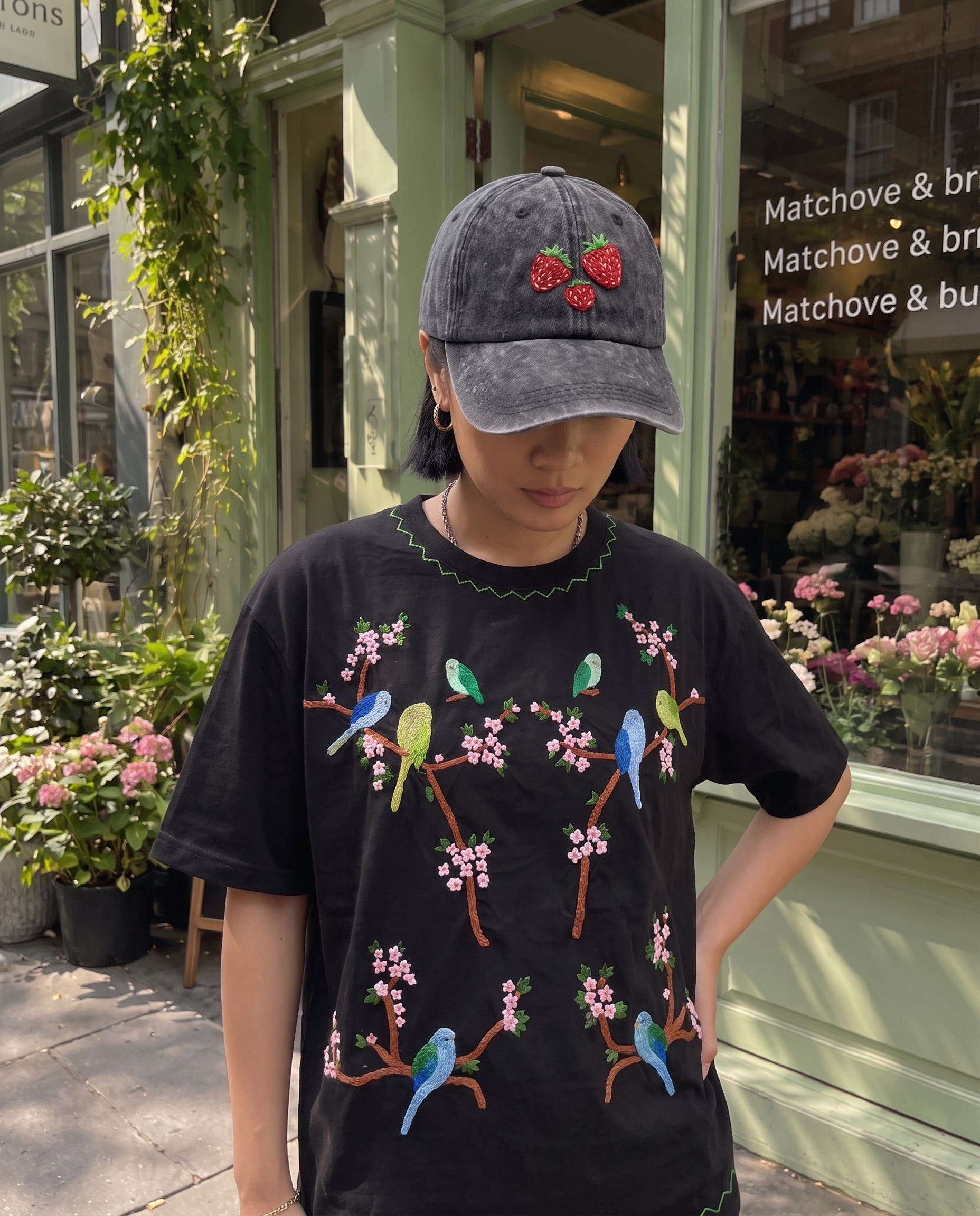 Strawberry embroidered cap worn outdoors with a hand-embroidered cherry blossom and parakeet t-shirt