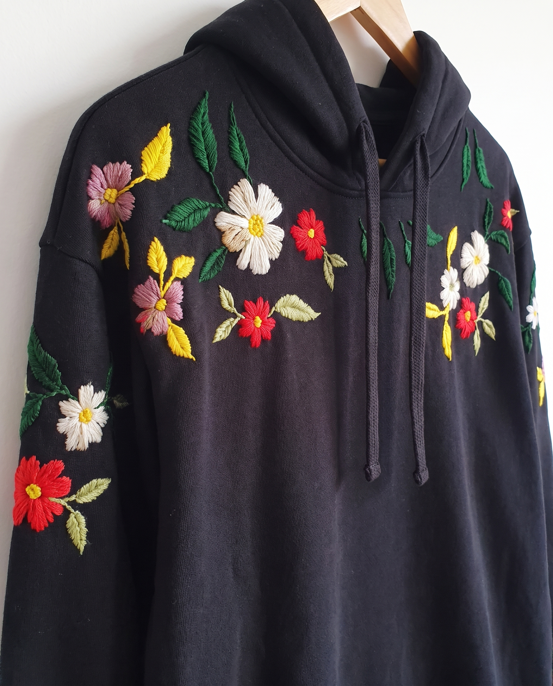 Angled view of the floral embroidered black hoodie showing the drawstring hood and flowers running down the sleeve